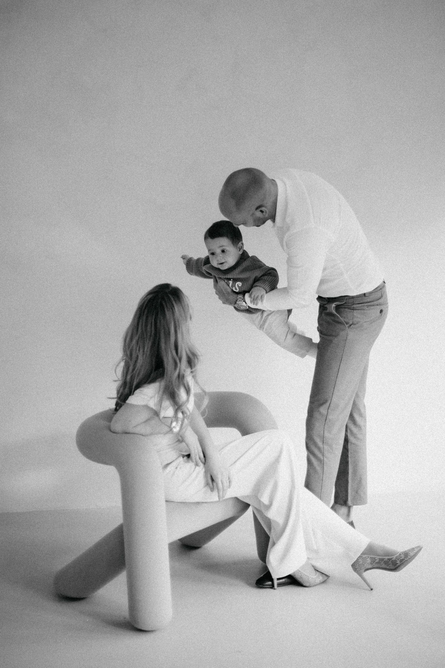 An intimate black and white family portrait showing playful interaction with a baby.
