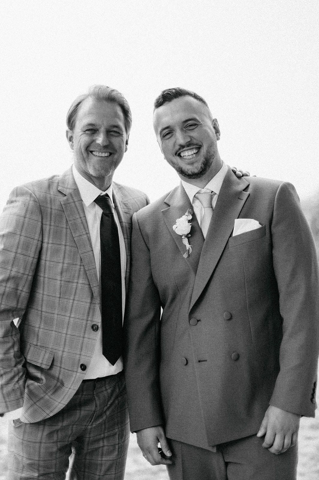Groomsmen in stylish suits share laughs during wedding photo session against white background.