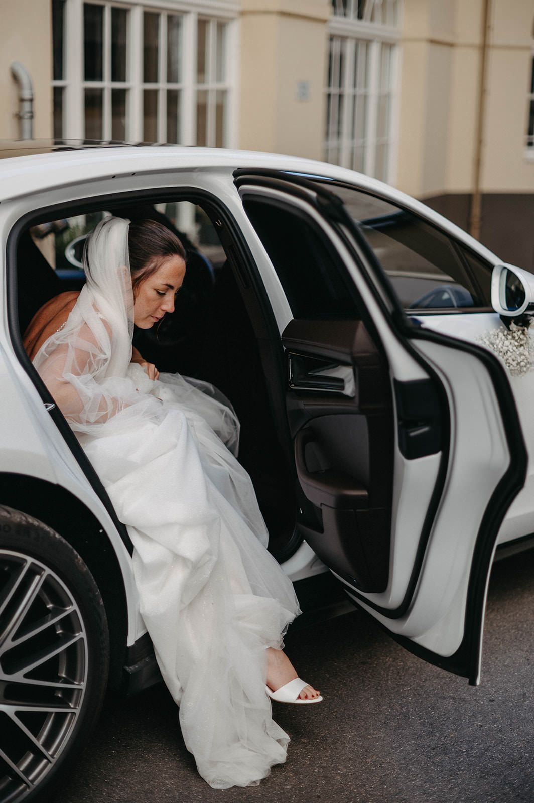 A bride in a white wedding dress carefully steps out of a luxury white car in a series of sequential photos.