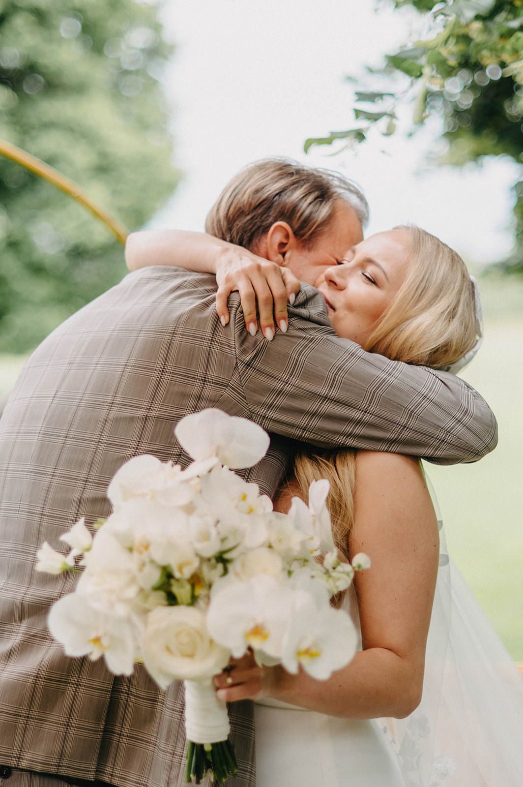 A tender embrace between newlyweds with a beautiful white orchid and rose bouquet at an outdoor wedding ceremony.
