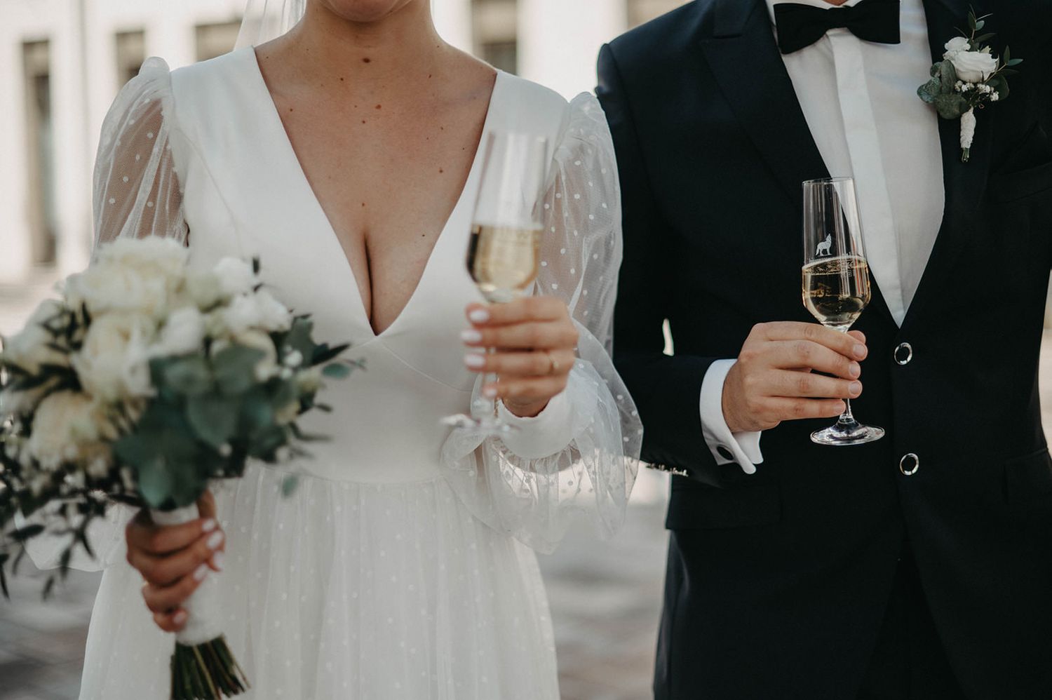 Wedding party members hold champagne glasses and bouquets while wearing formal attire at an elegant celebration.