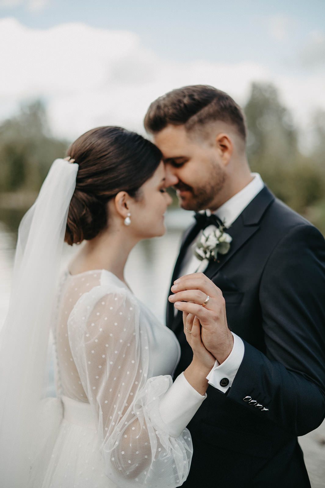 Romantic wedding couple shares intimate moment in elegant black and white attire against soft outdoor backdrop.