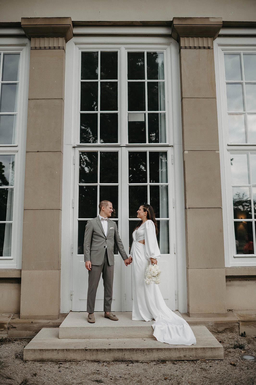 A wedding couple shares a tender first look moment in front of elegant white windows on their special day.