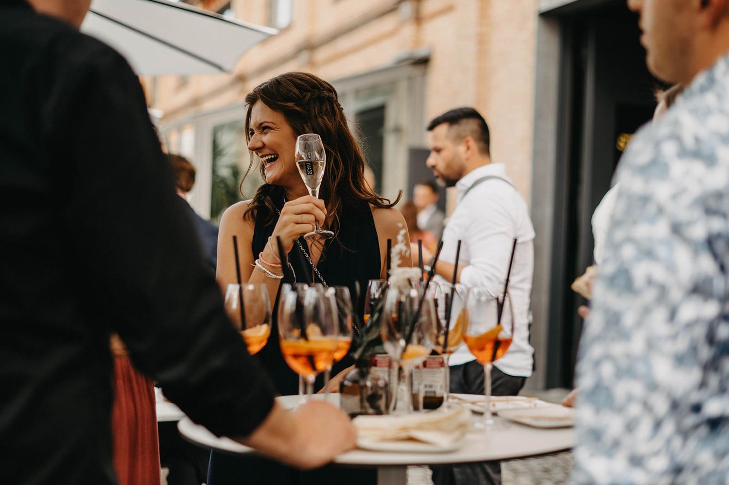 People enjoying aperol spritz cocktails at an outdoor cafe terrace on a sunny day.