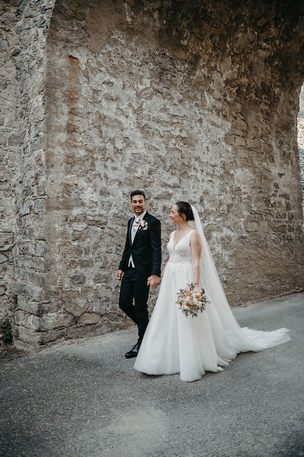 A bride and groom share an intimate moment against a rustic stone wall in an artistic black and white wedding photo series.