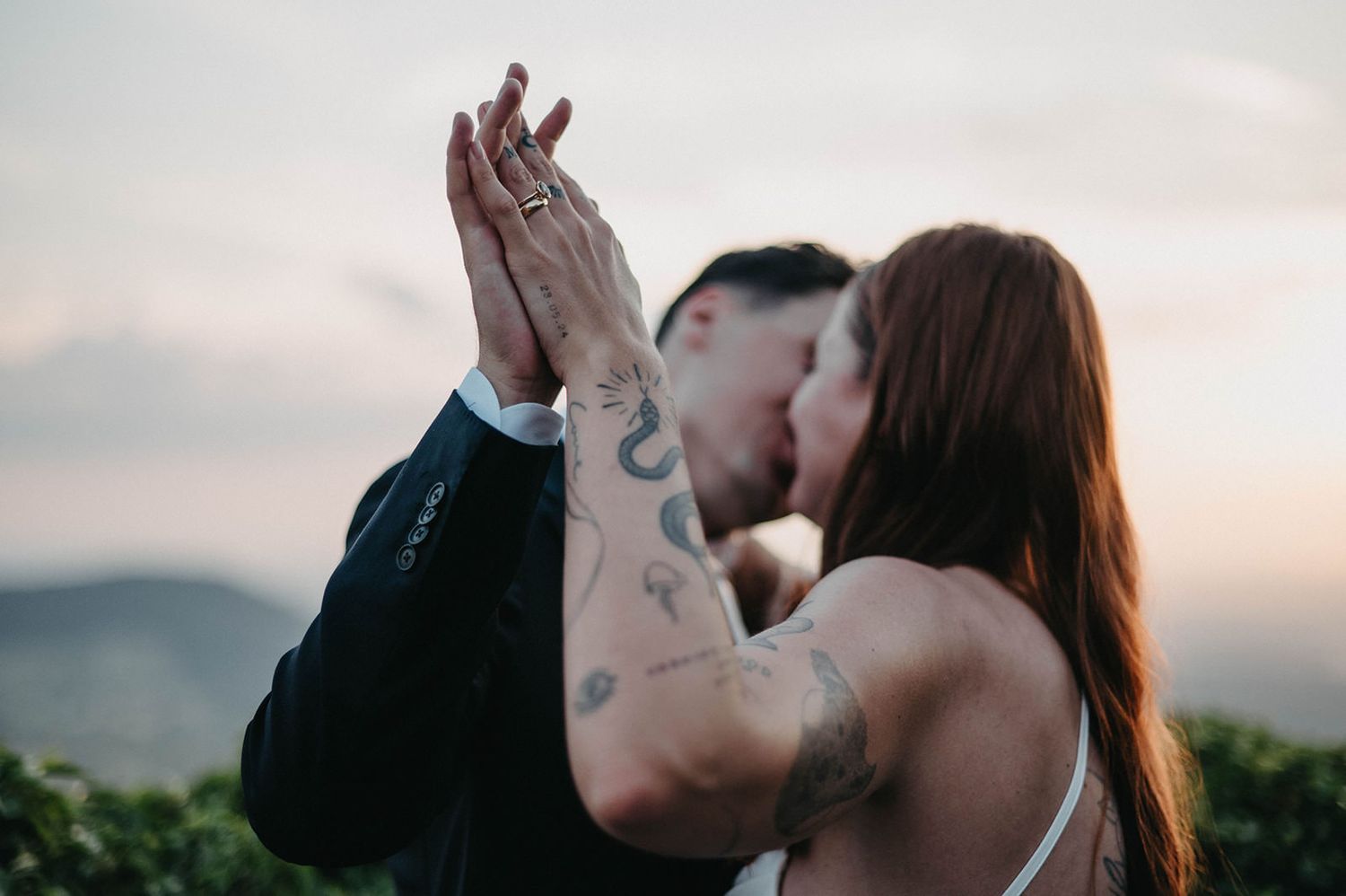 A couple shares a romantic kiss against a scenic mountain backdrop during sunset.