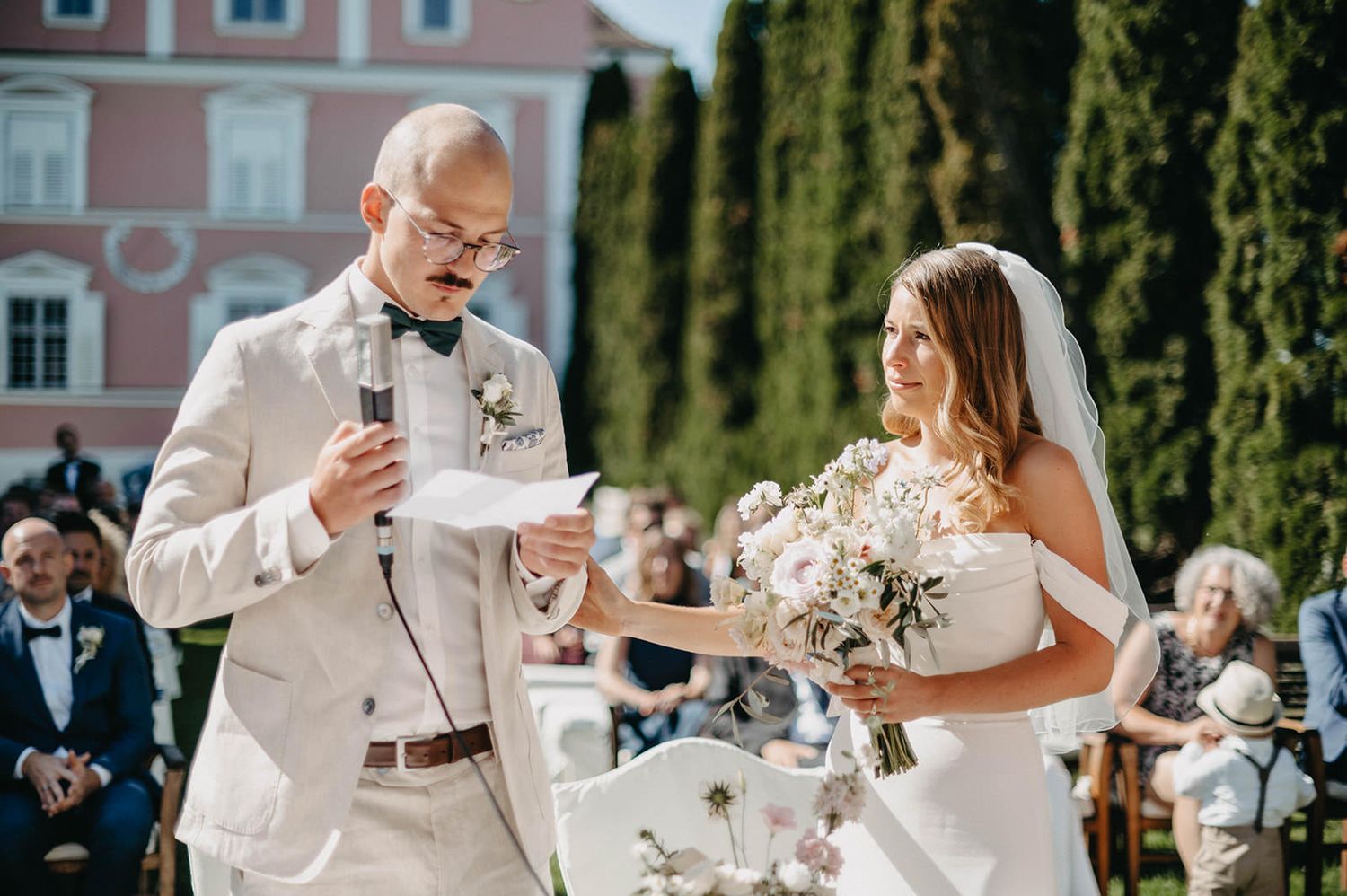 Elegant outdoor wedding reception with guests toasting at long tables adorned with floral arrangements in a garden setting.