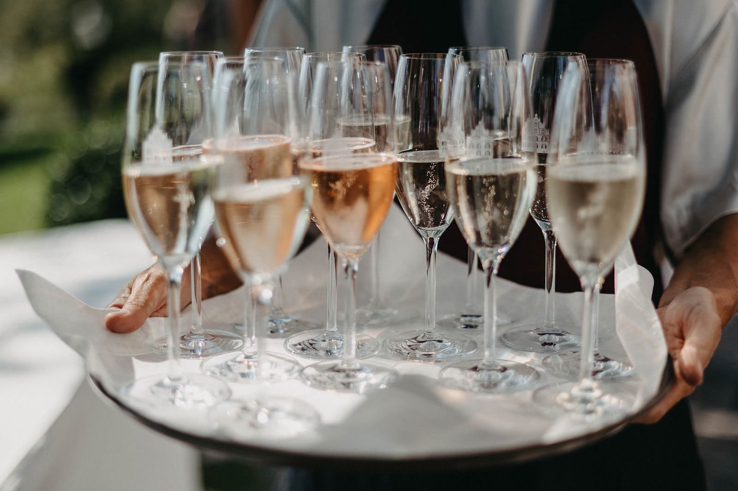 A silver tray holds multiple champagne flutes filled with rose wine being served at an outdoor event.