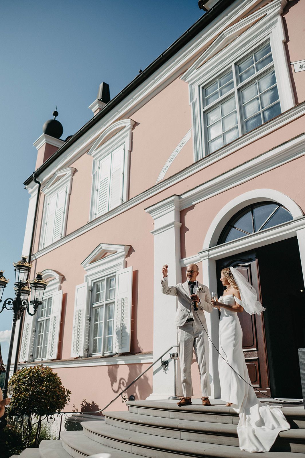 A series of joyful moments captured on the steps of a pink historic building with arched windows and elegant architecture.