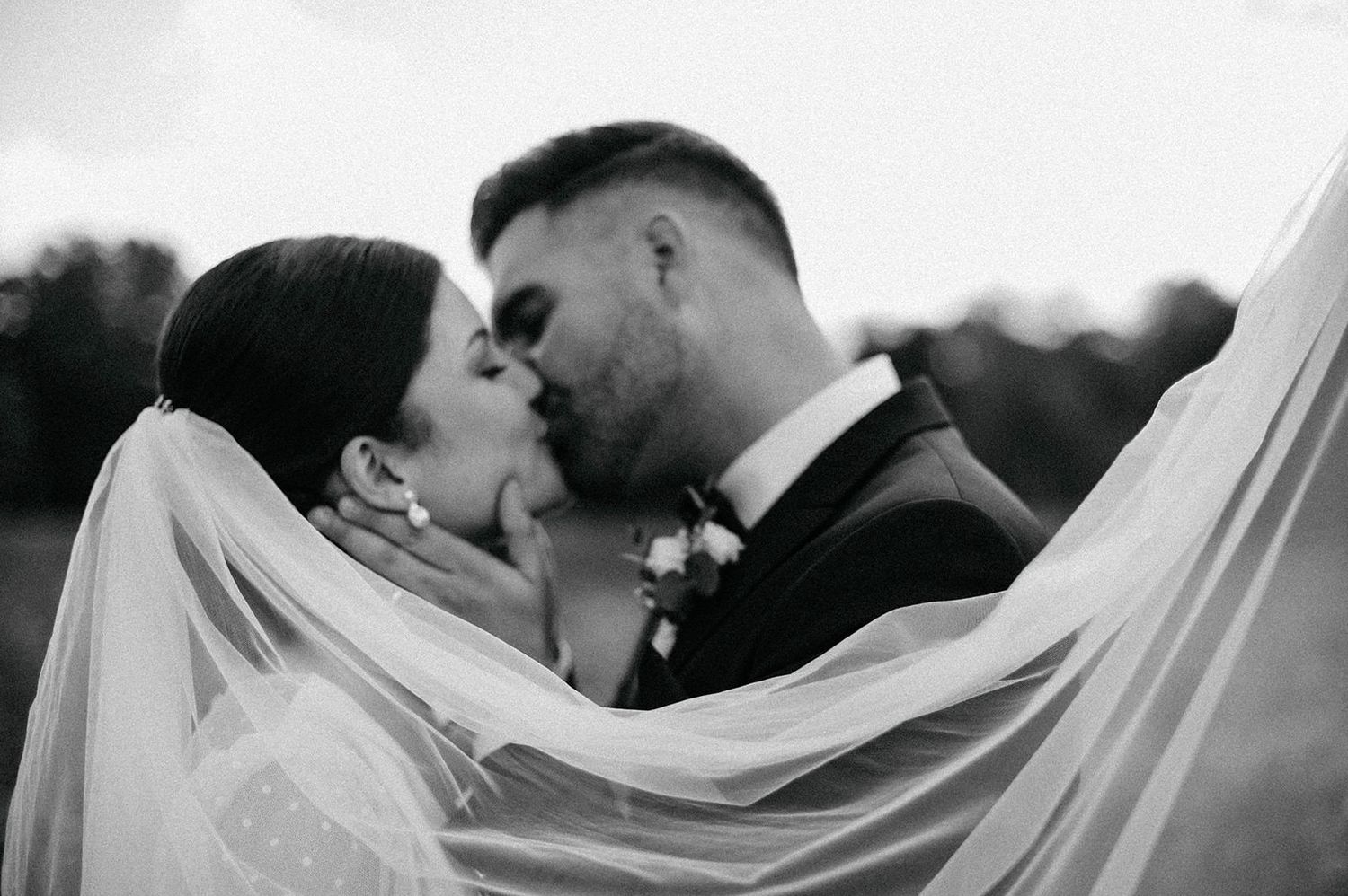 A romantic black and white wedding photo showing a tender kiss between newlyweds with a flowing white veil.