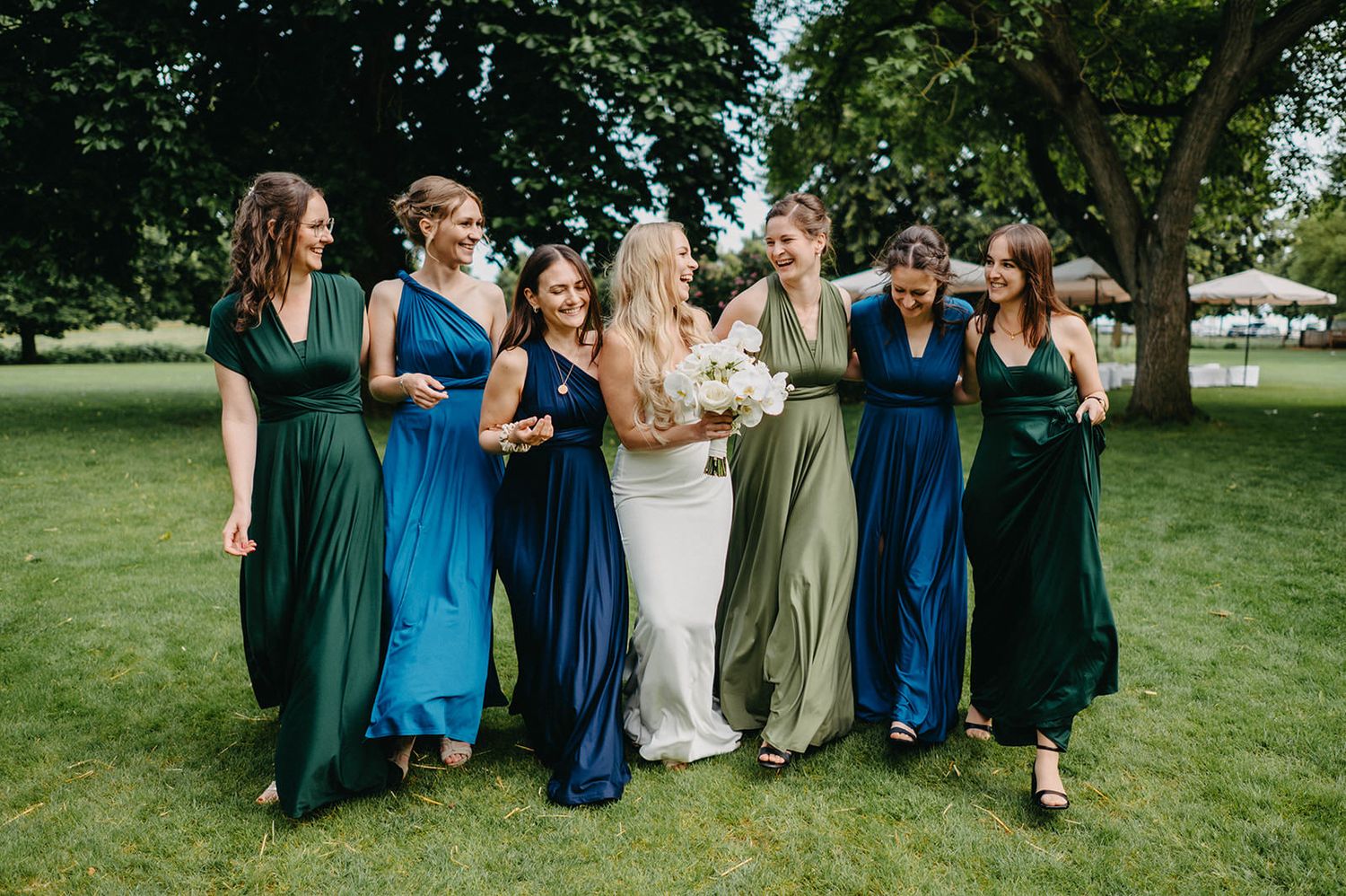 A group in coordinated blue and green formal attire walks together on a grassy lawn during an outdoor event.