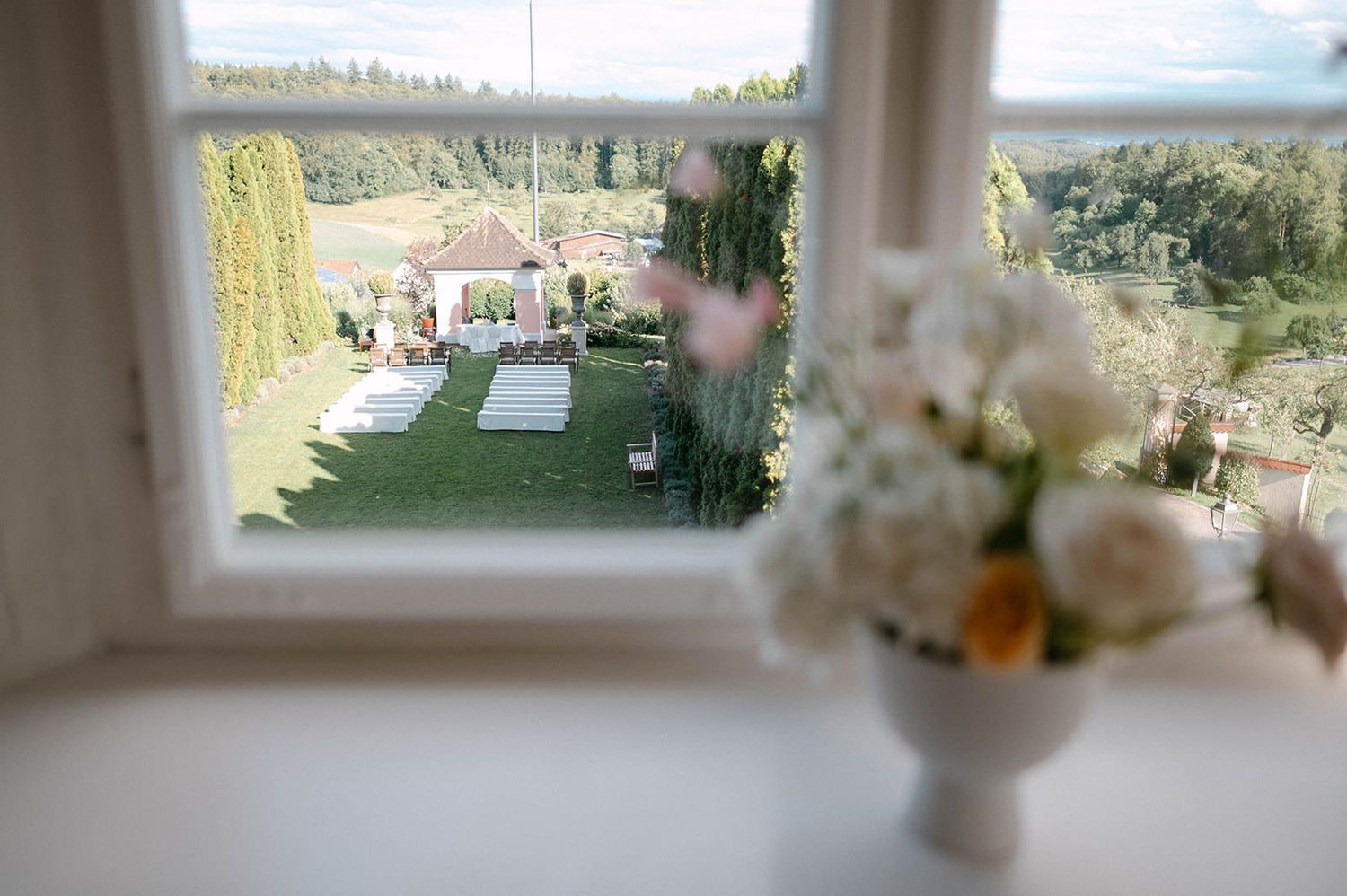 Panoramic view of a garden wedding ceremony setup with white chairs and mountain landscape in the background.