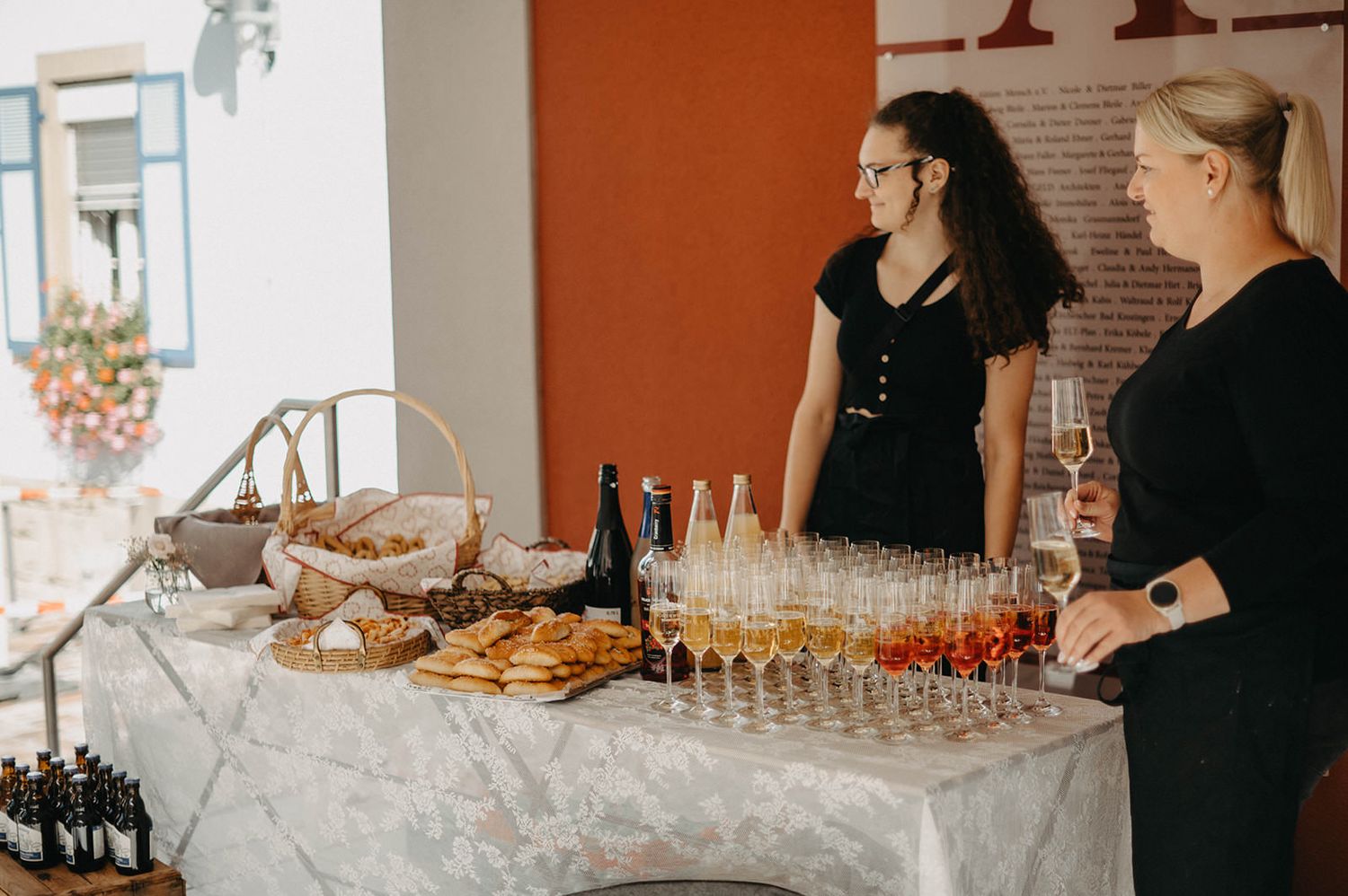 Catering staff prepare food and drinks at an elegant event with appetizers and beverages displayed on tables.