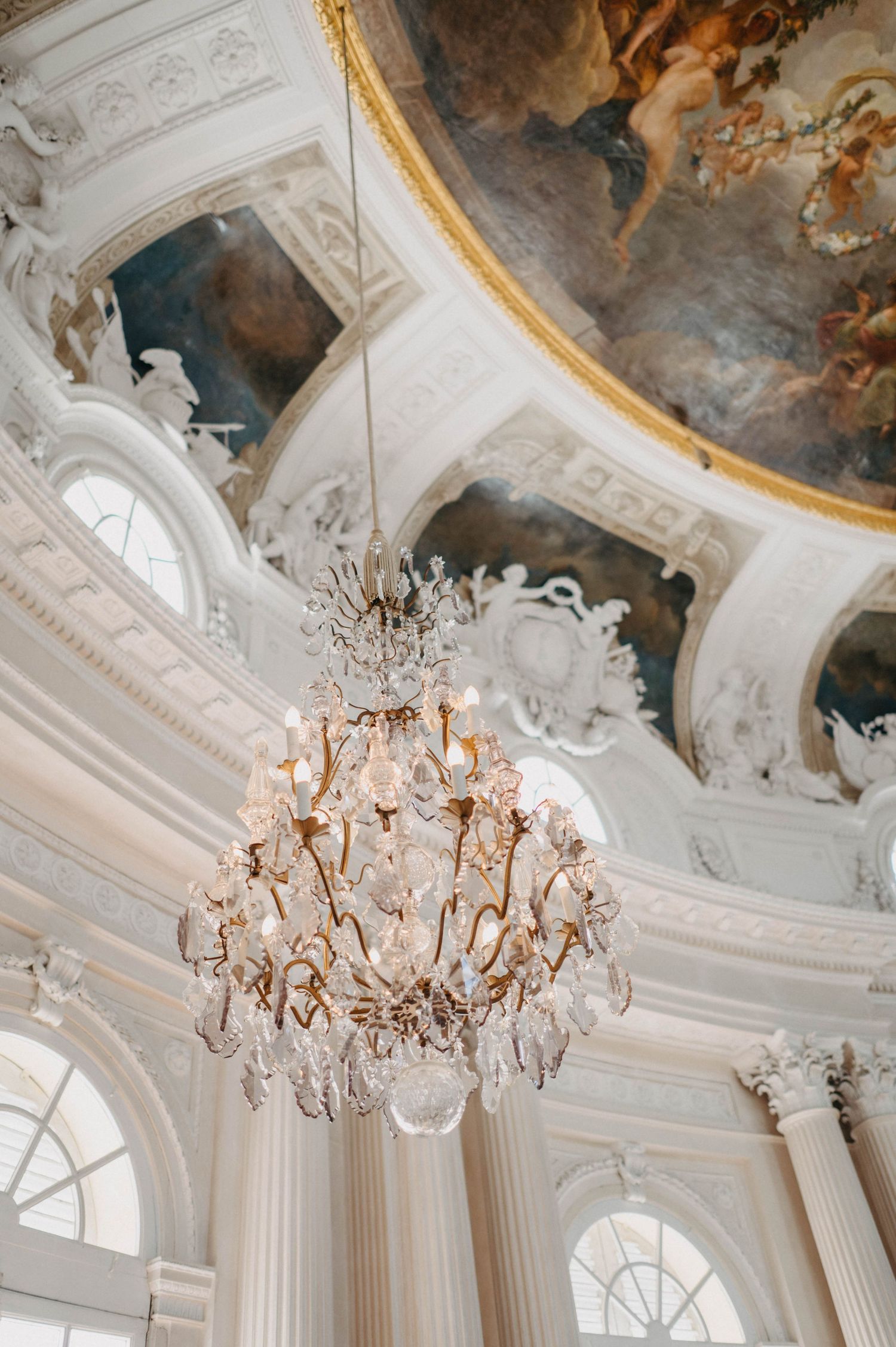 Ornate baroque ceiling with crystal chandeliers and white architectural details in a palatial setting.