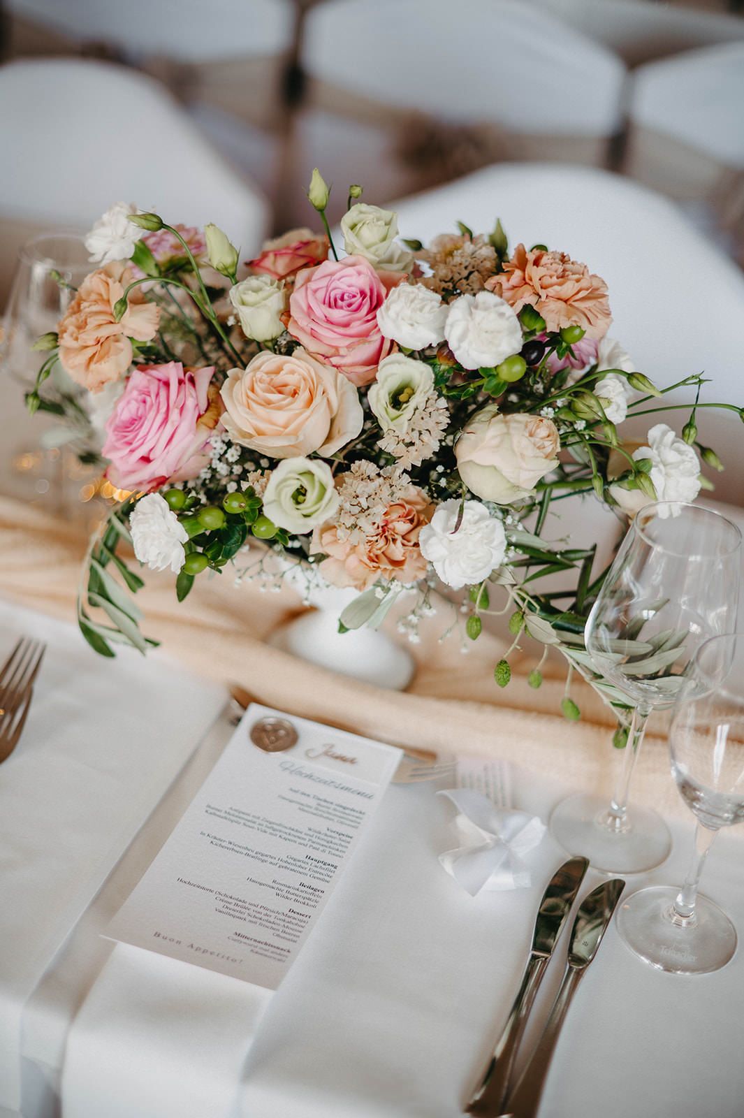 Elegant wedding table setting with pink and peach floral centerpieces, white linens, and menu cards.