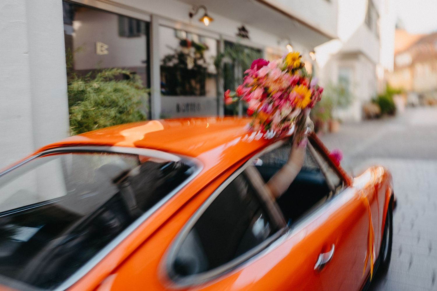 Orange sports car with floral bouquet on top being driven down a street with motion blur effect.