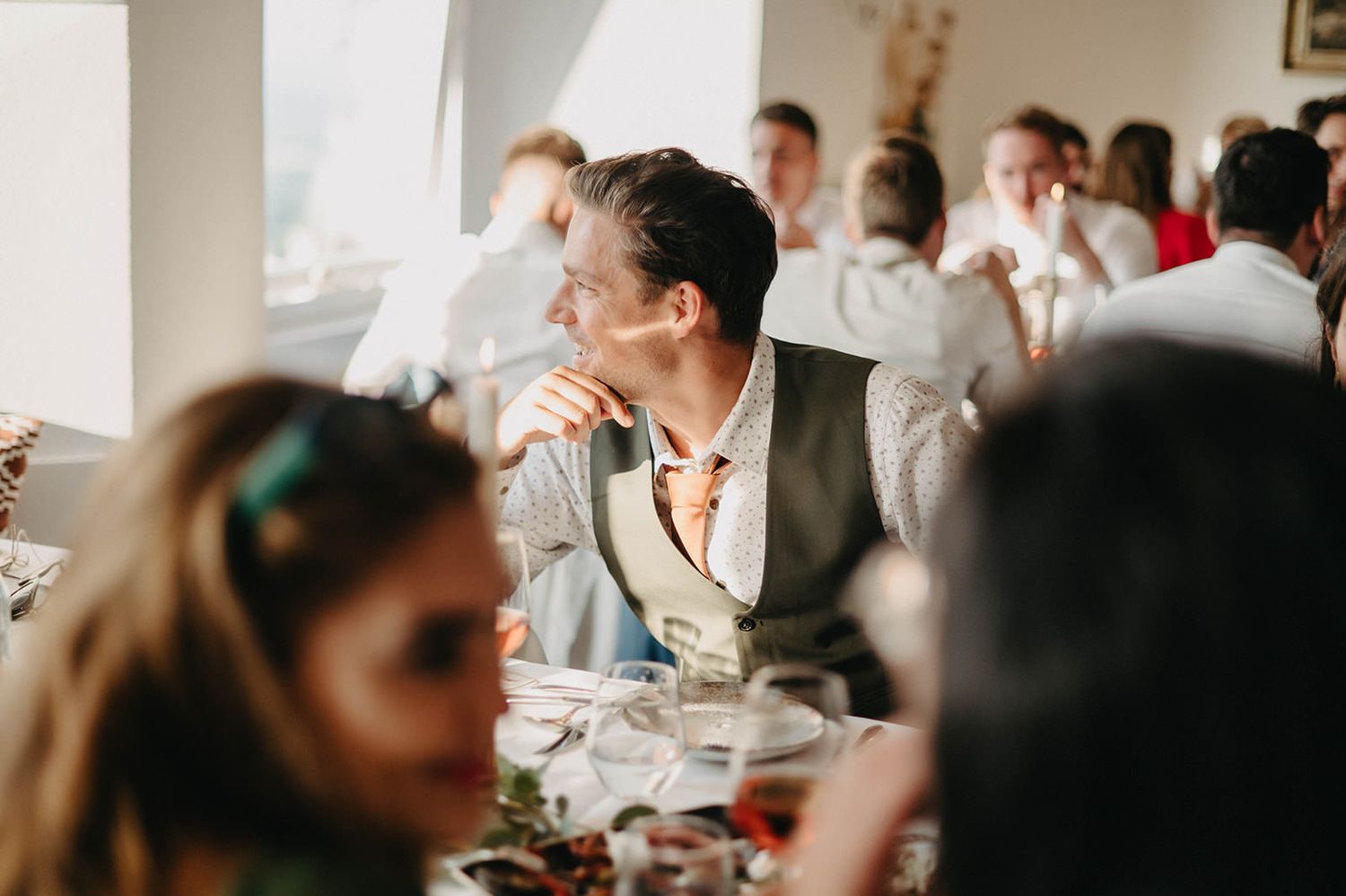 Guests seated at elegant tables during a wedding reception enjoy conversation and drinks in a bright indoor venue.