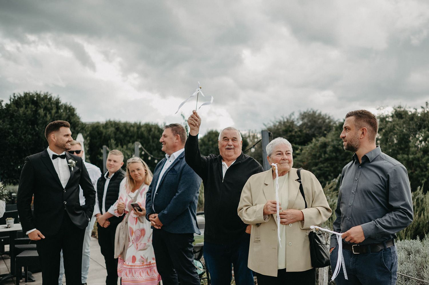 Wedding guests gather outdoors under cloudy skies for a celebration event.