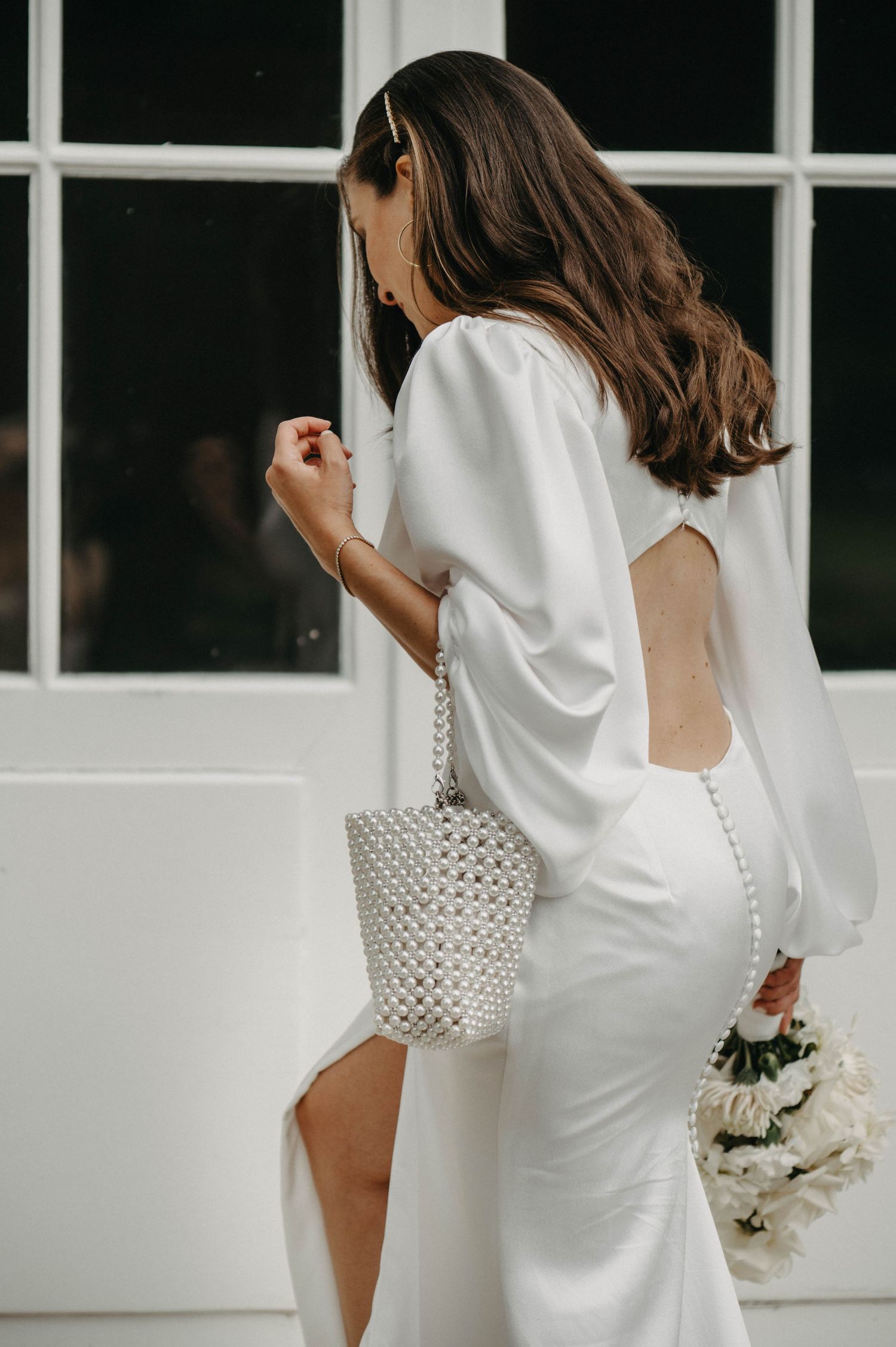 Bride in modern white dress with puffy sleeves and beaded handbag seen from behind.
