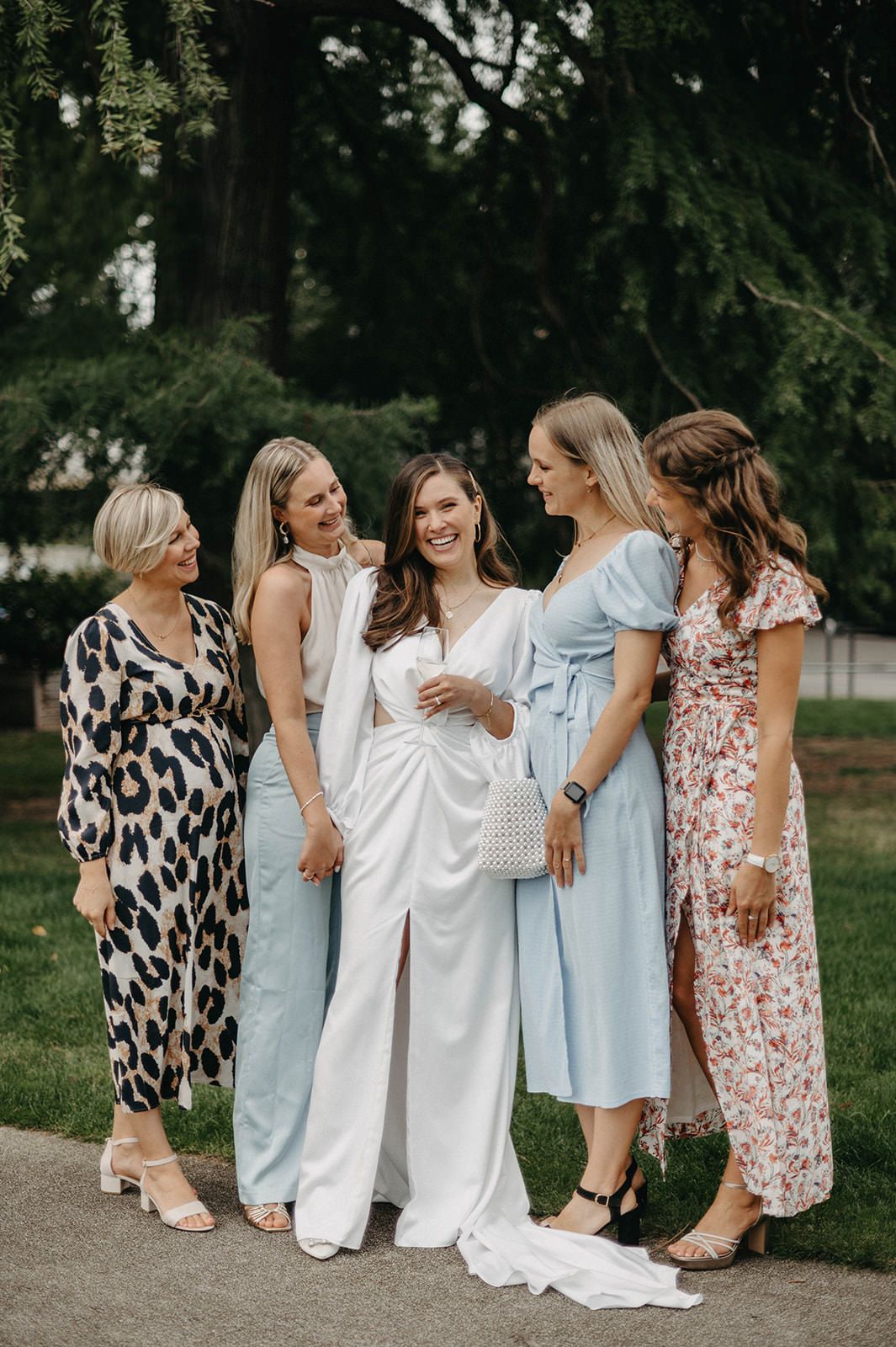 A group of women in elegant dresses gather outdoors for a wedding celebration in a garden setting.