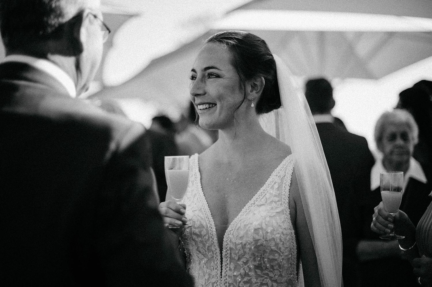 A bride in a lace V-neck wedding dress and veil smiles joyfully during her wedding reception.