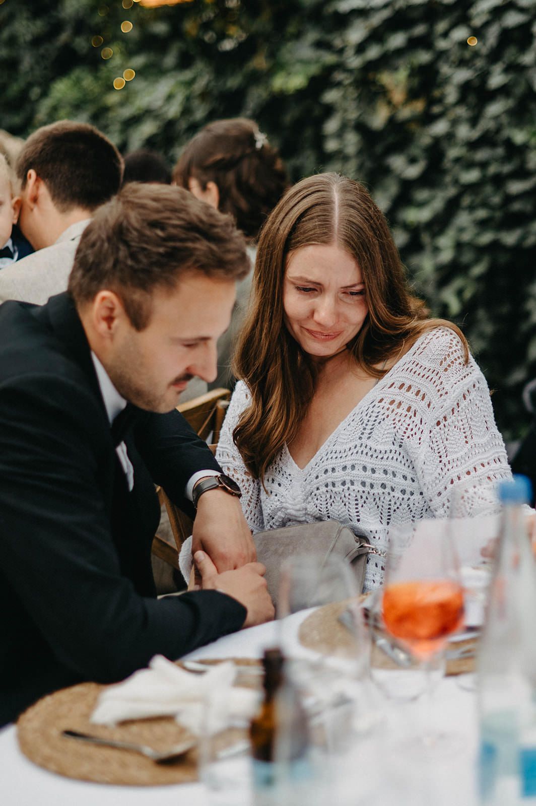 A couple shares an intimate moment at an outdoor dining table with drinks and place settings.