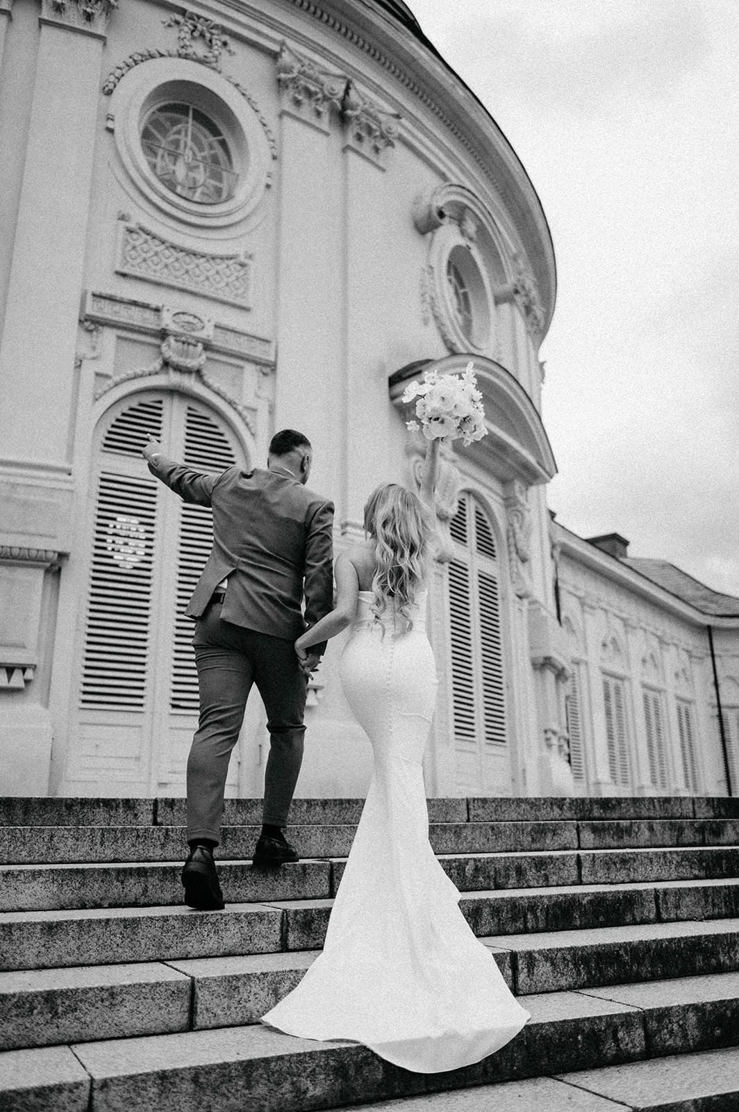 Black and white wedding photos showing a bride and groom ascending elegant stone steps at a historic building.
