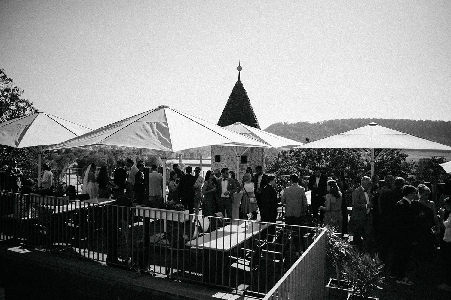 Black and white panoramic view of a crowded outdoor event with tents and railings against a cloudy sky.