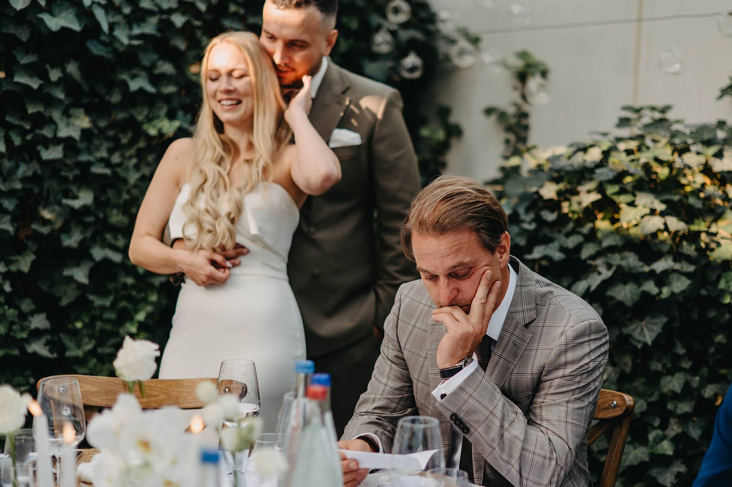 Candid moment at a wedding reception shows guests sharing laughter and emotions at an outdoor table setting.