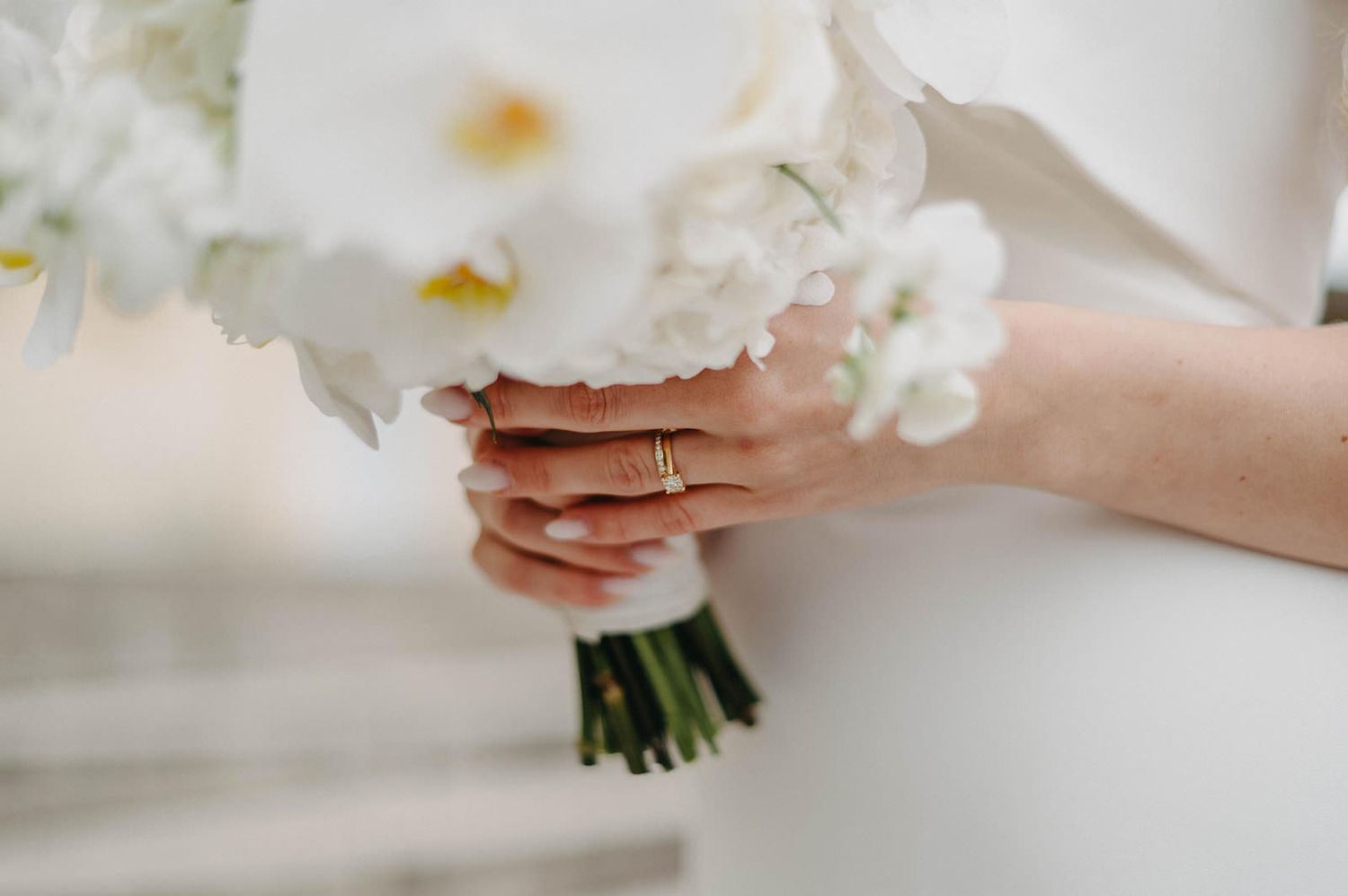 A white wedding bouquet with delicate flowers and ribbons is held against a light background.
