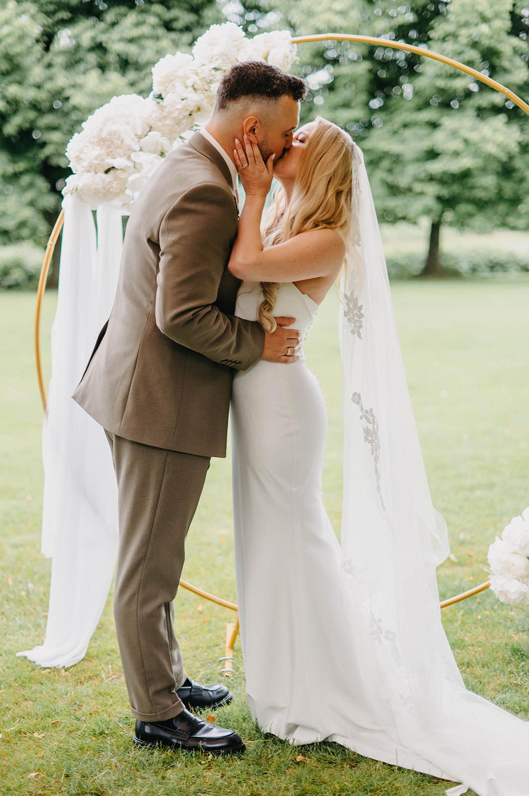 Romantic outdoor wedding ceremony with a circular arch decorated in white flowers and flowing fabric.