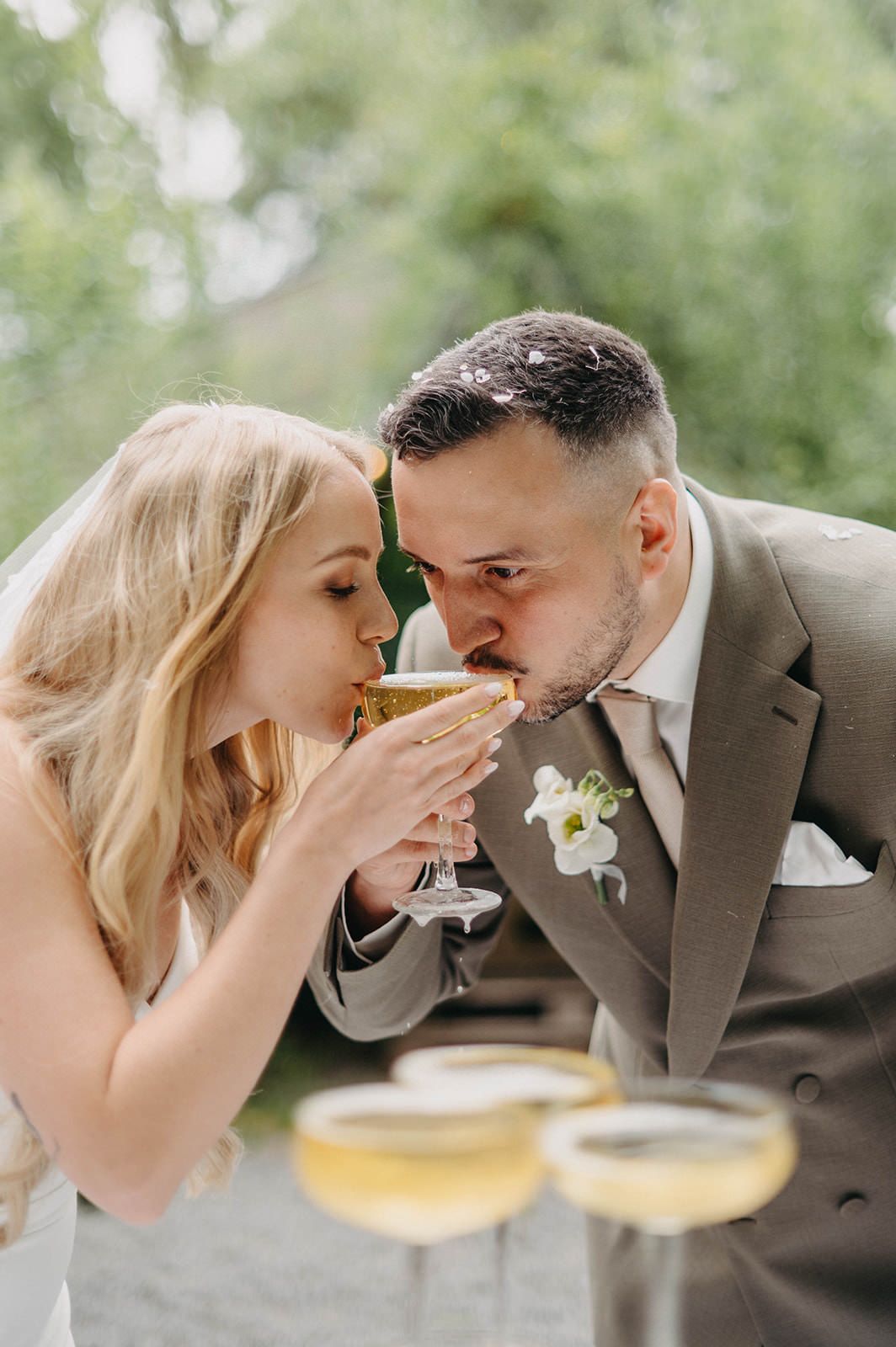 Couple playfully sharing drinks through straws at an outdoor wedding reception.