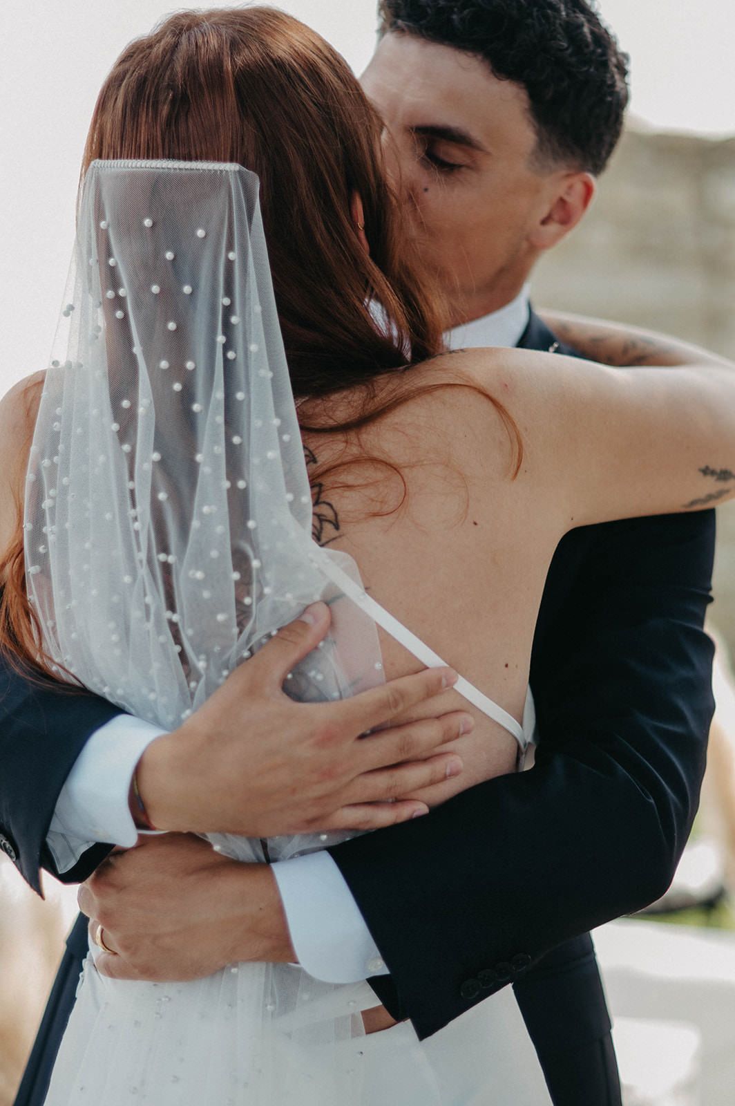 A romantic wedding couple embraces in a series of intimate photos showing the bride's delicate pearl-dotted veil.