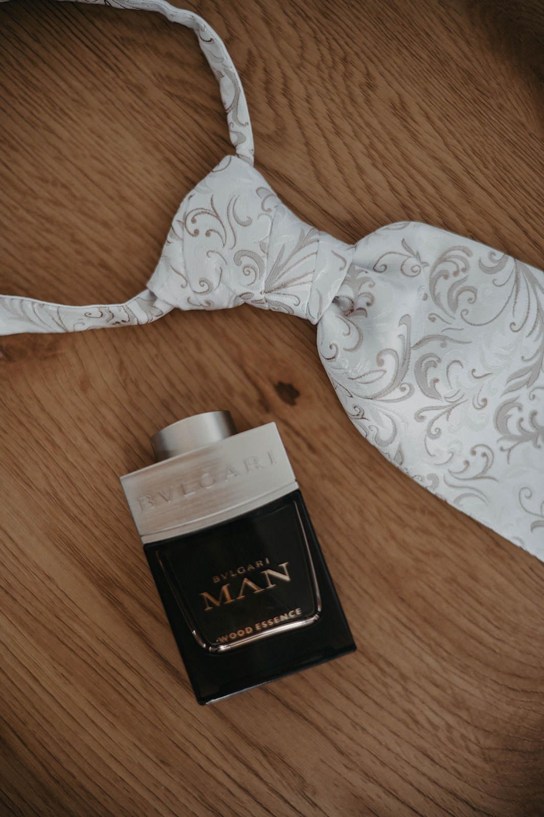 A white lace patterned bra and black Bvlgari Man perfume bottle arranged on wooden surface.