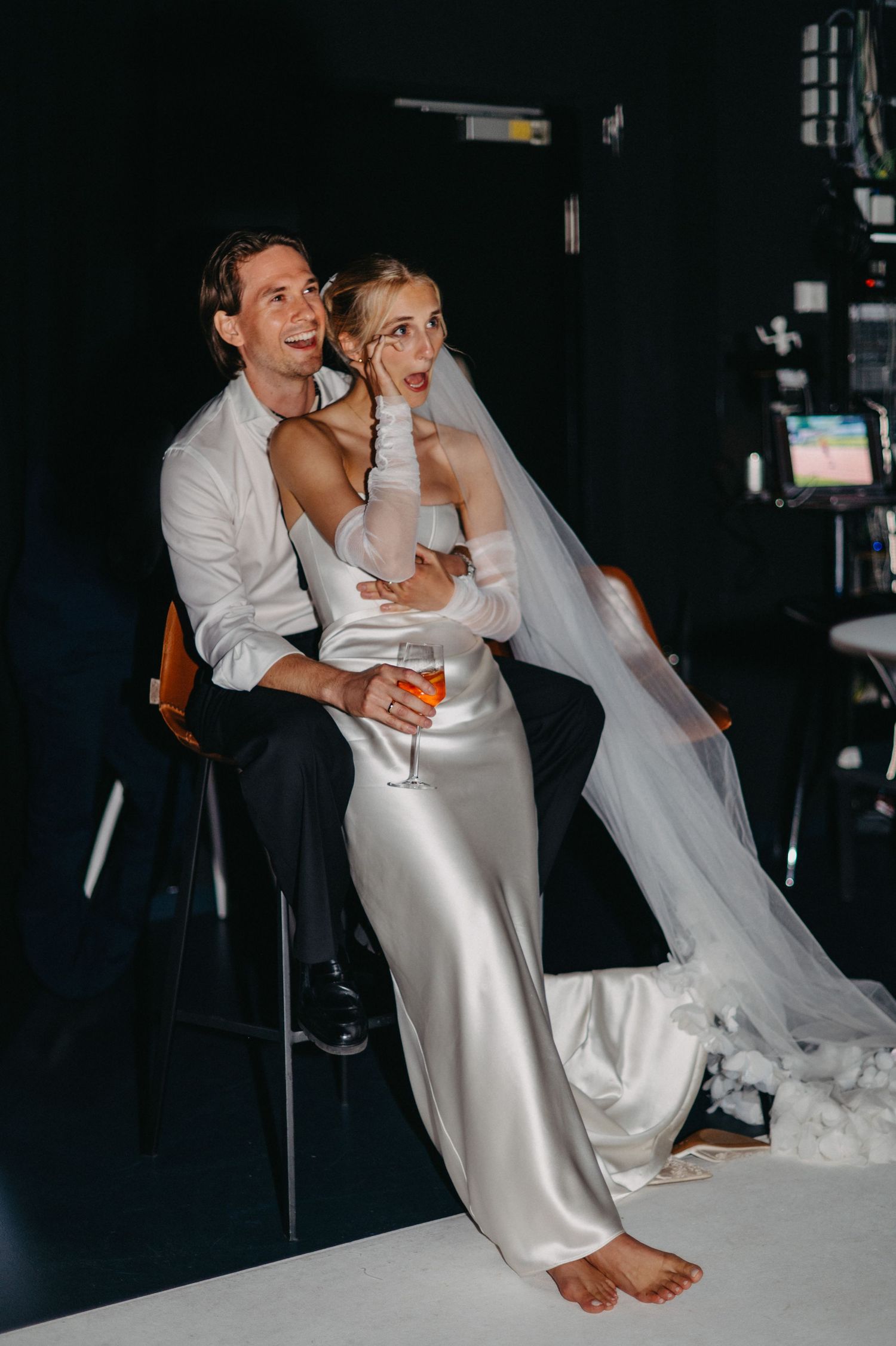 A couple in wedding attire shares intimate moments while sitting together at their reception.