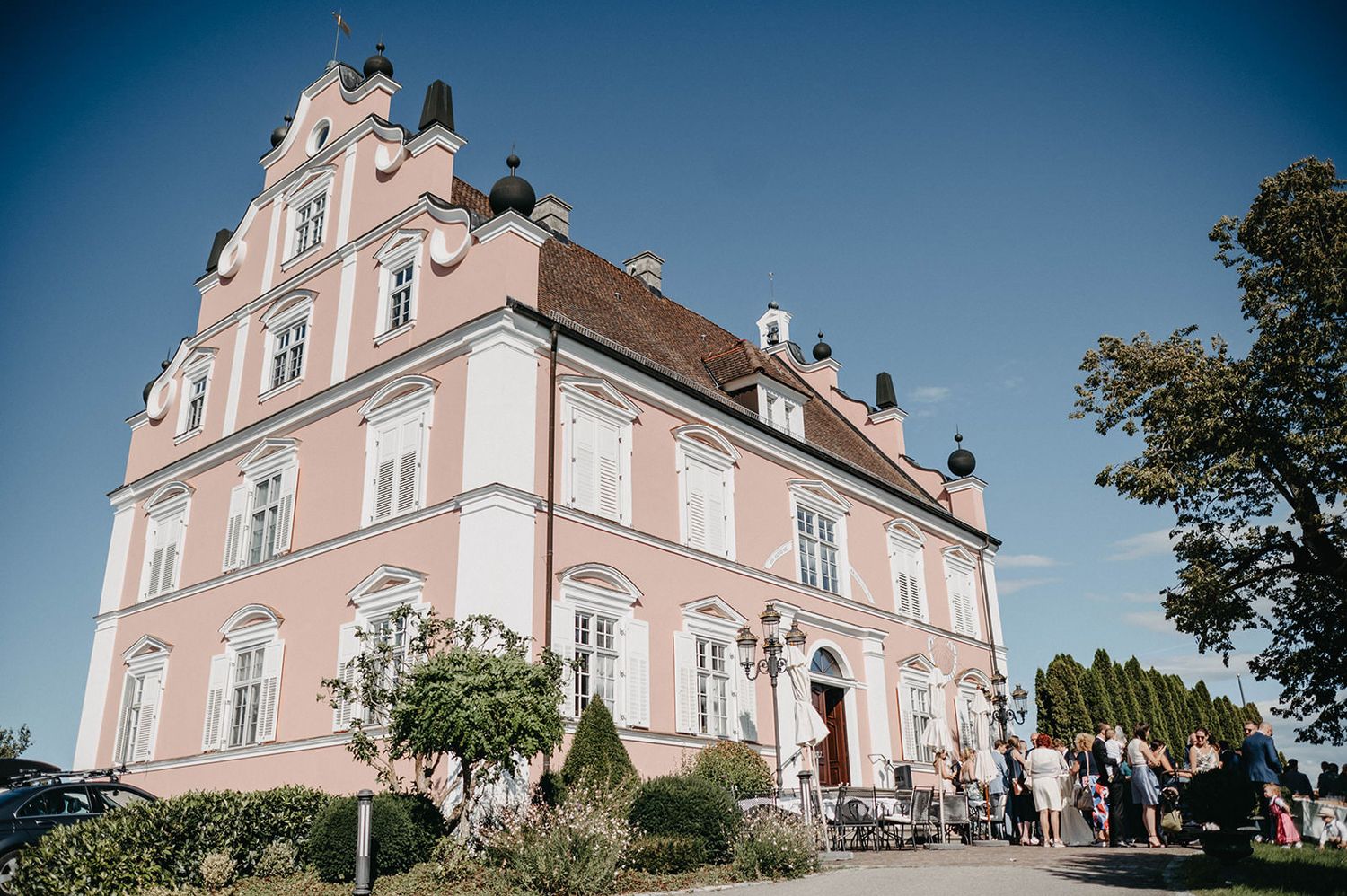 Elegant pink baroque-style mansion with ornate architecture and grand entrance stands against blue sky on sunny day.