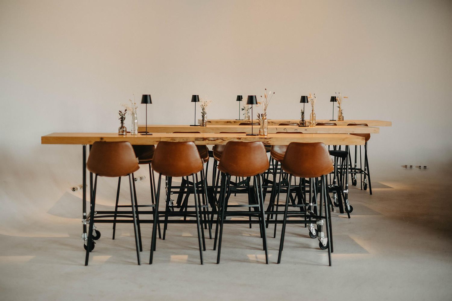 Wooden tables and black metal chairs arranged in rows create a minimalist dining or classroom setup.