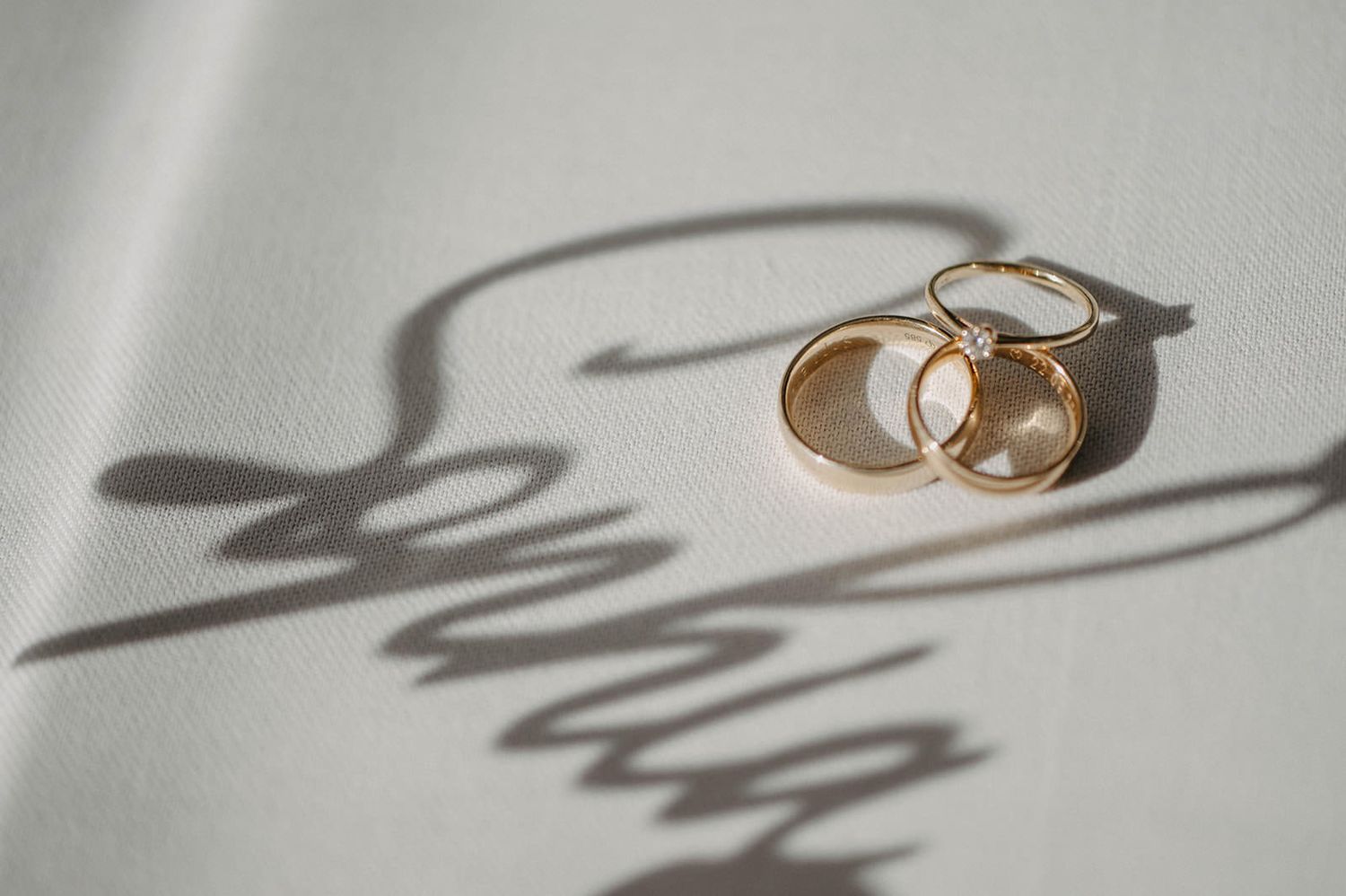 A pair of gold wedding rings casting shadows on a white surface in dramatic lighting.