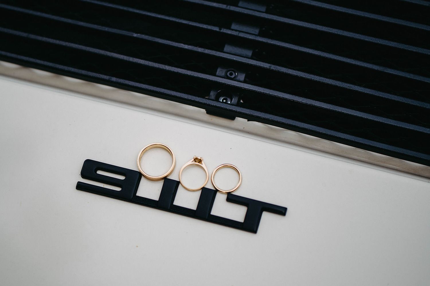 Vintage Porsche 911 badge with gold wedding rings creatively arranged on the lettering against a white surface.