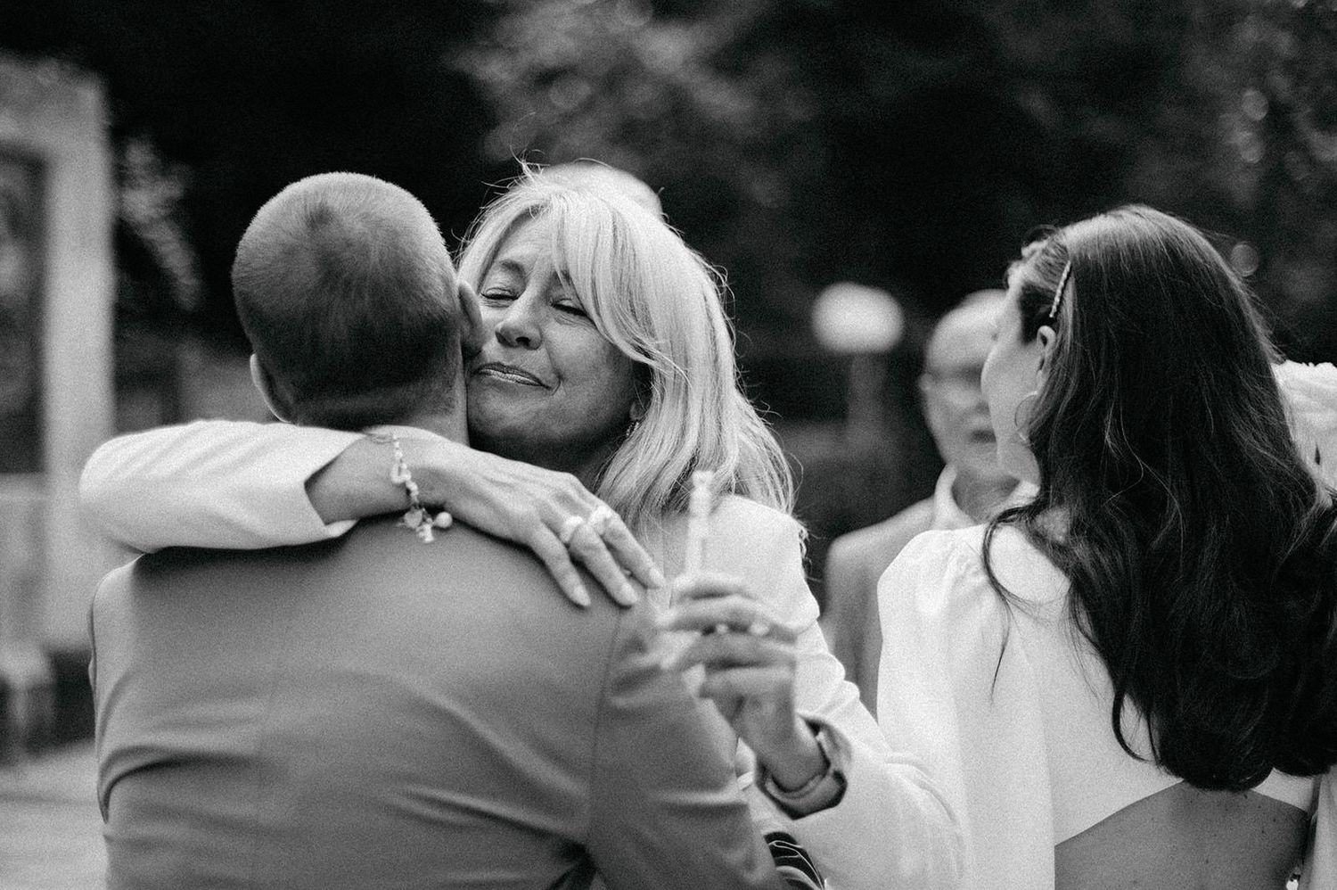 Black and white photo of wedding guests sharing emotional embraces during a celebration.