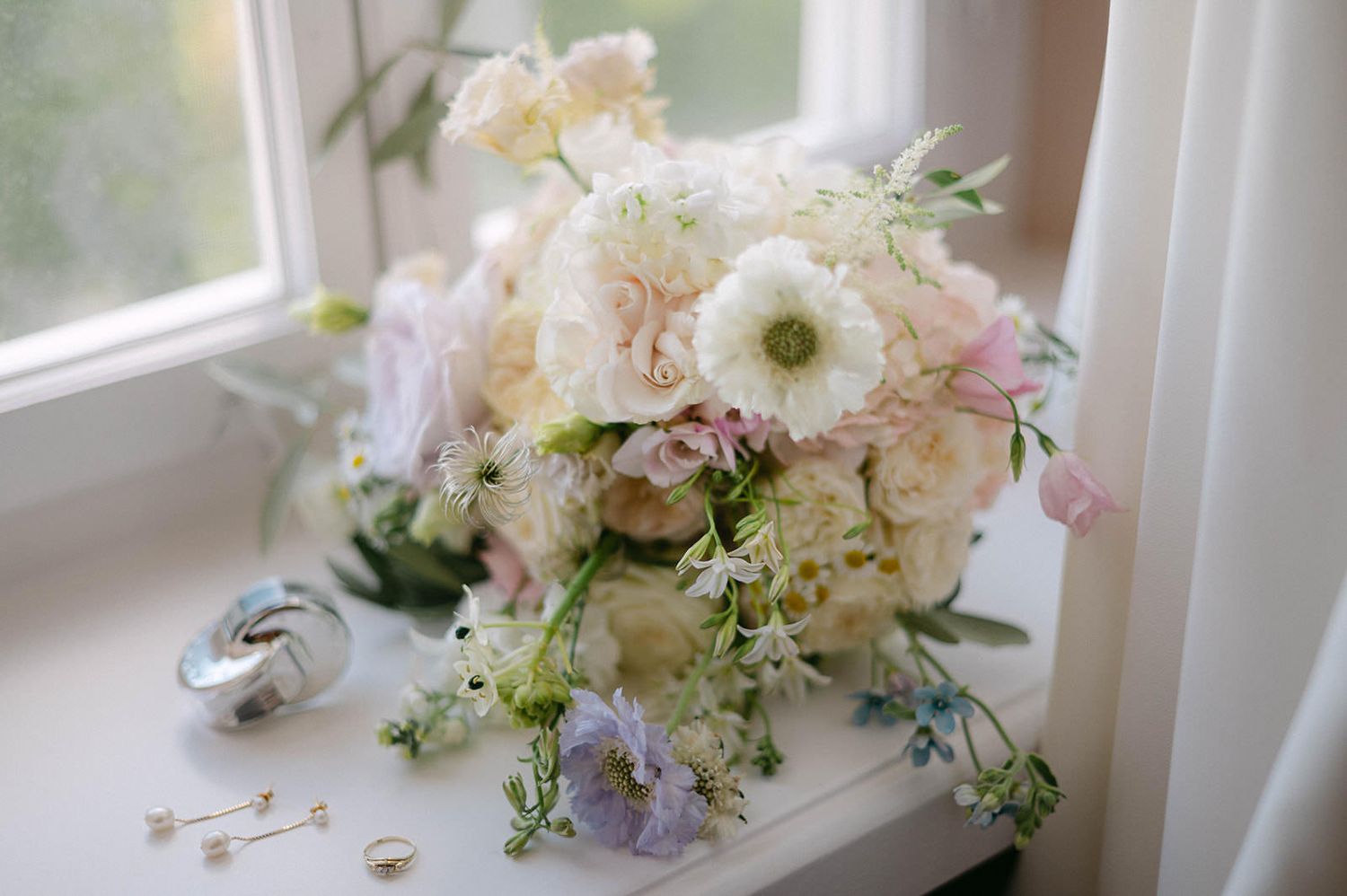 Elegant white and blush floral arrangements with roses and delicate greenery displayed near a window.