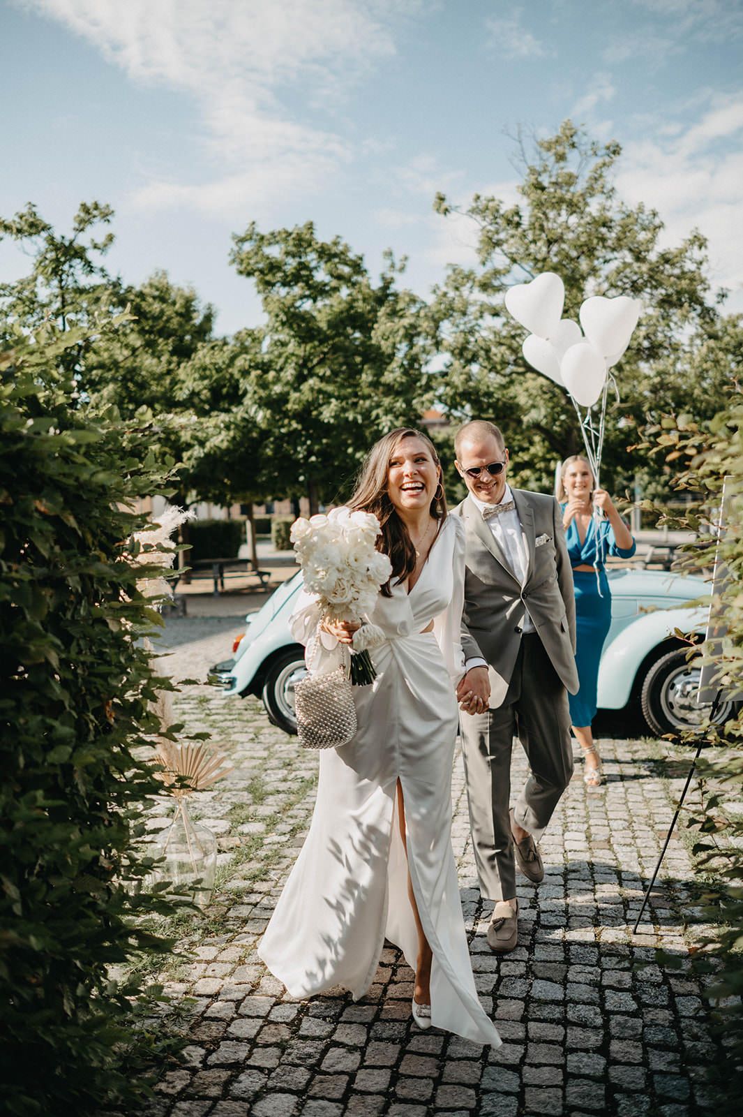 A wedding celebration on a cobblestone path with a vintage blue Volkswagen Beetle in the background.