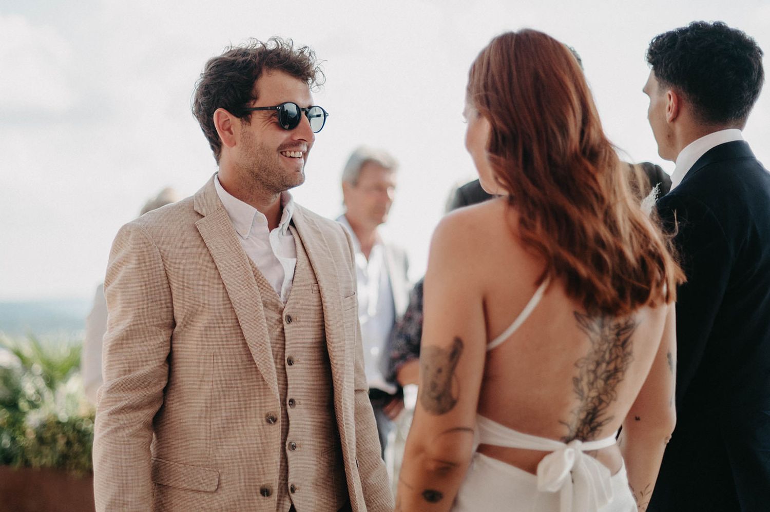 Wedding guests mingle and socialize during an outdoor reception on a sunny afternoon.