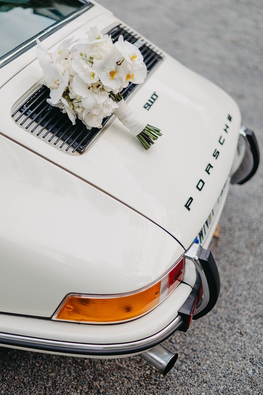 Close-up details of a white vintage Porsche car with headlights and a delicate white floral bouquet on top.