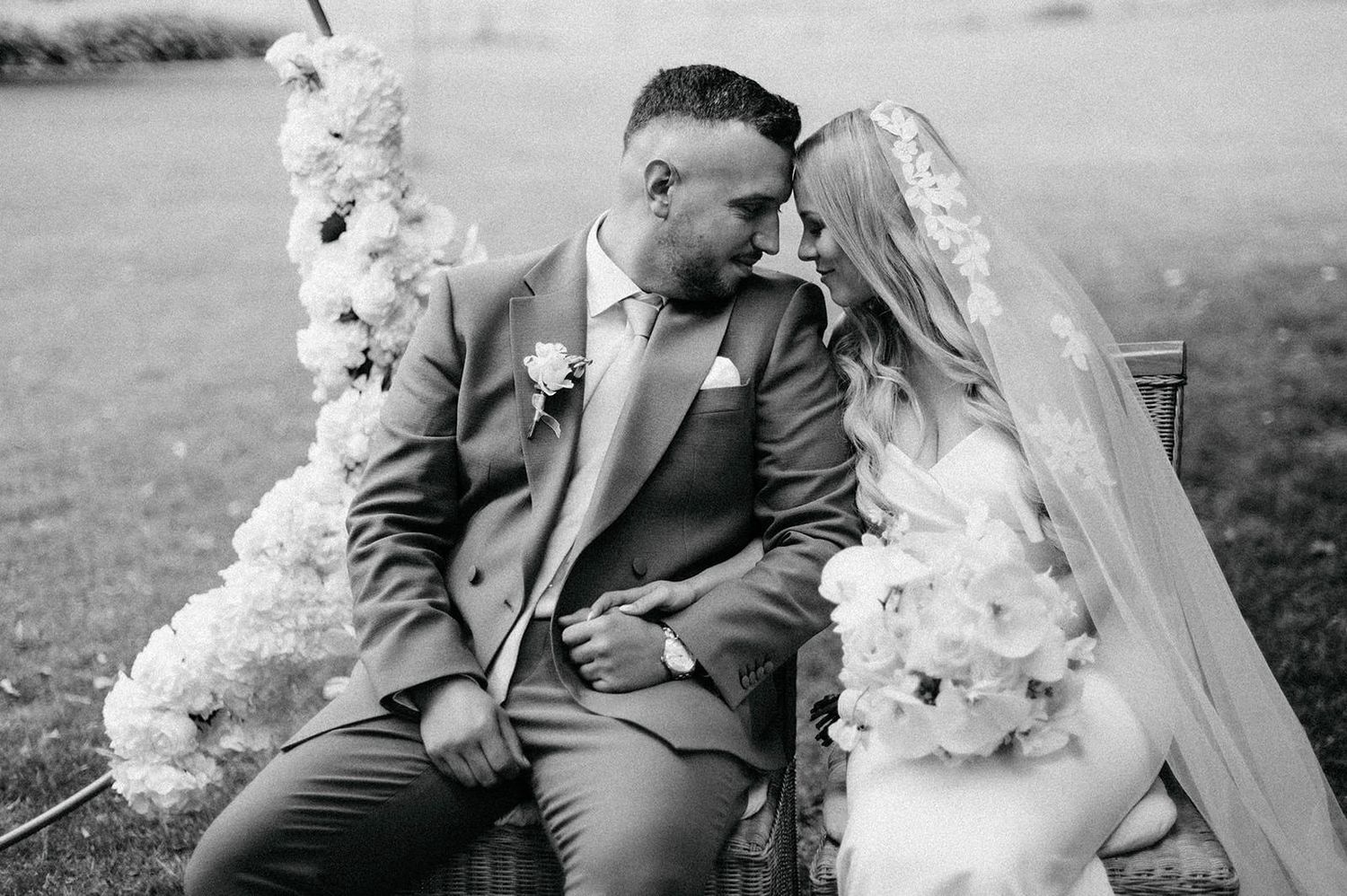 A romantic black and white portrait of newlyweds sitting close together with floral decorations.