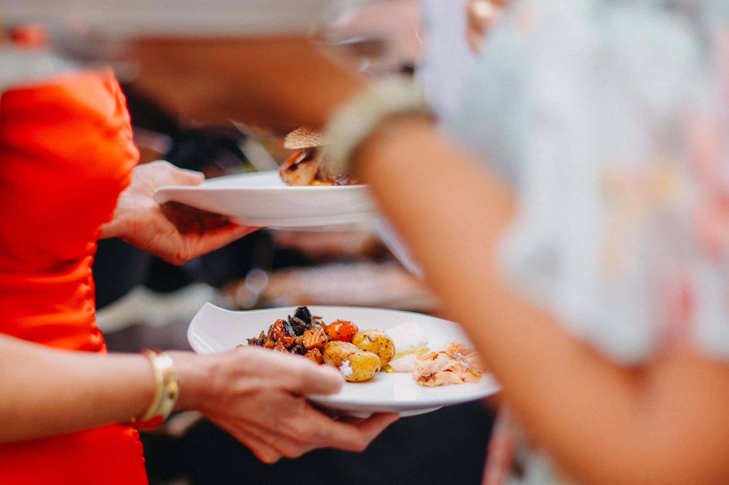 A close-up view of hands passing plates of food across a table during a shared meal.