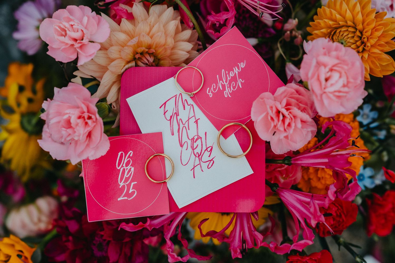 Pink and orange flowers arranged with bright fuchsia wedding place cards and calligraphy details.
