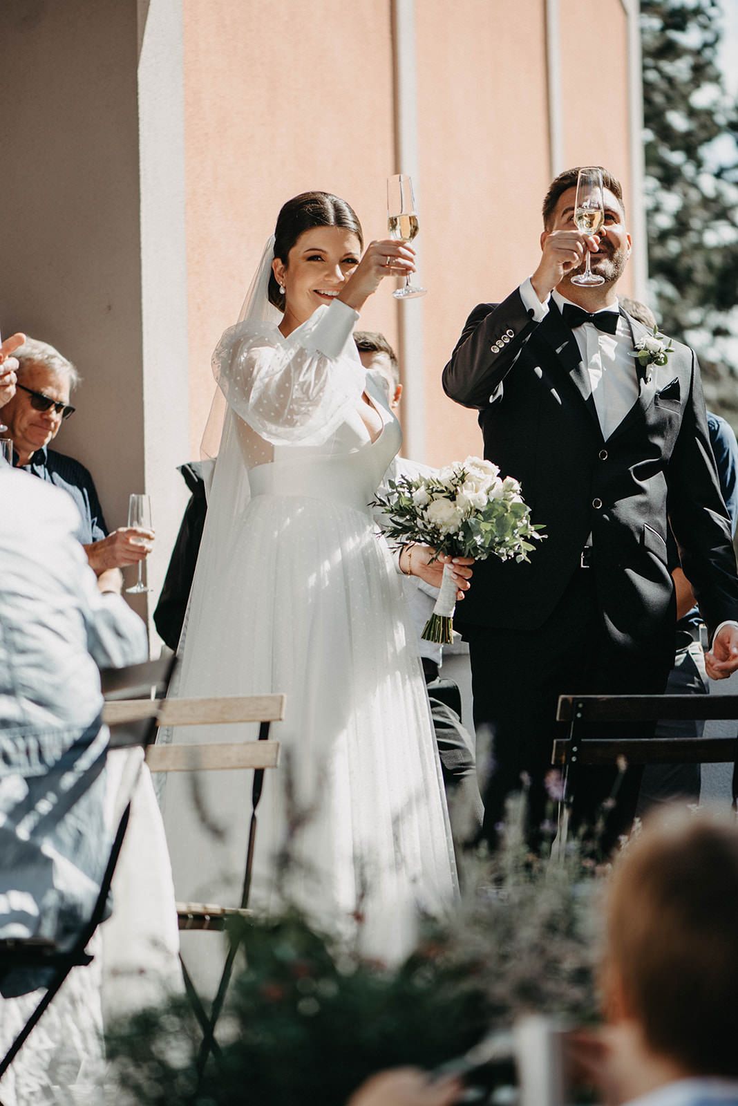 Newlyweds raise their wine glasses in a celebratory toast during an outdoor wedding ceremony.
