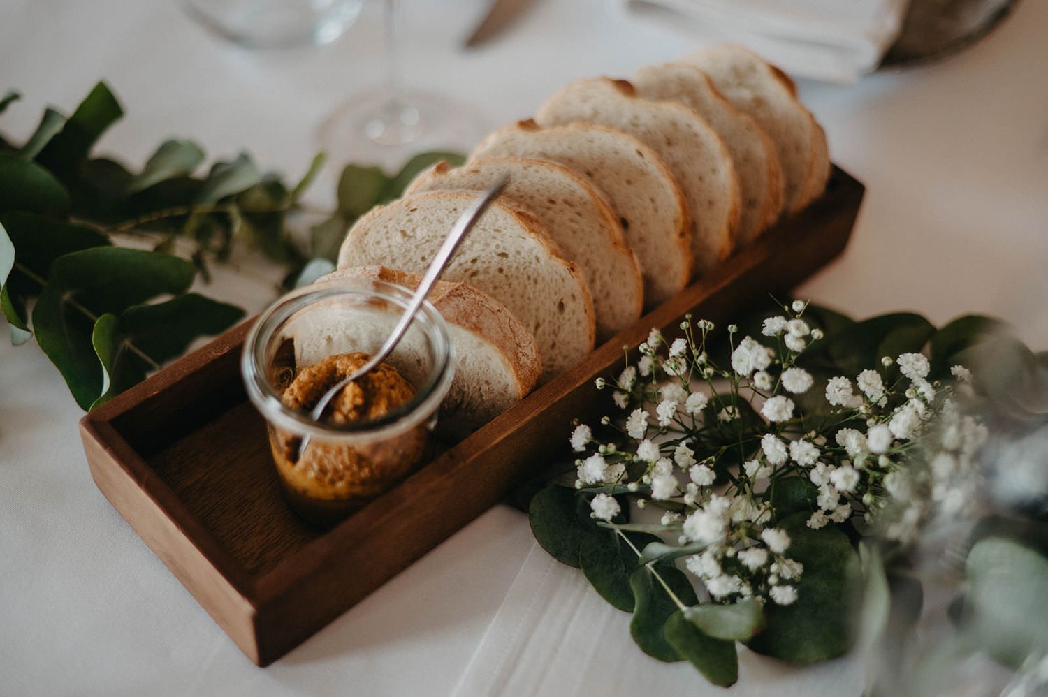 Sliced rustic bread served on wooden board with baby's breath flowers and greenery table decoration.