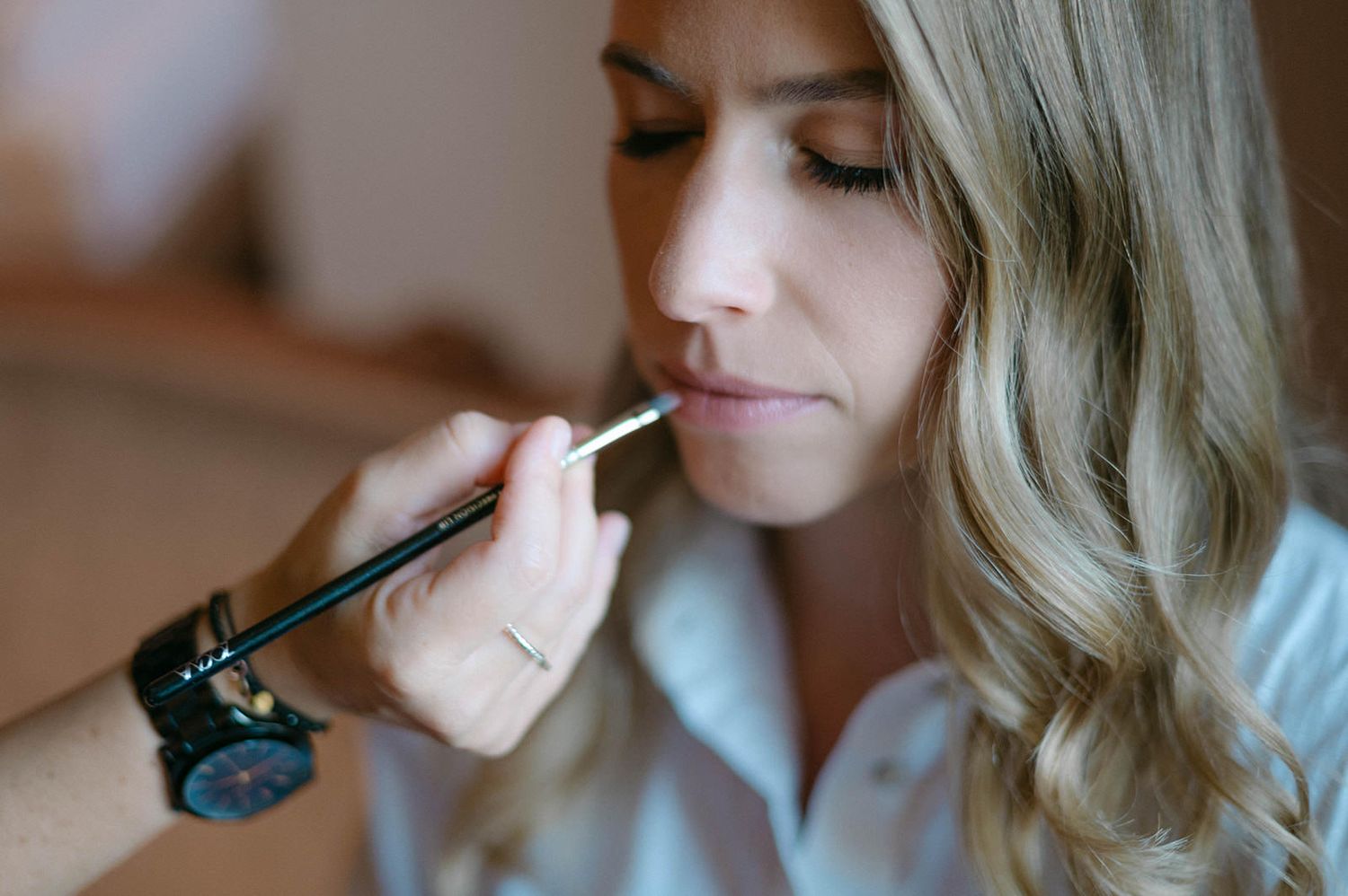 Black and white photo series showing makeup application and wedding day preparations near a window.